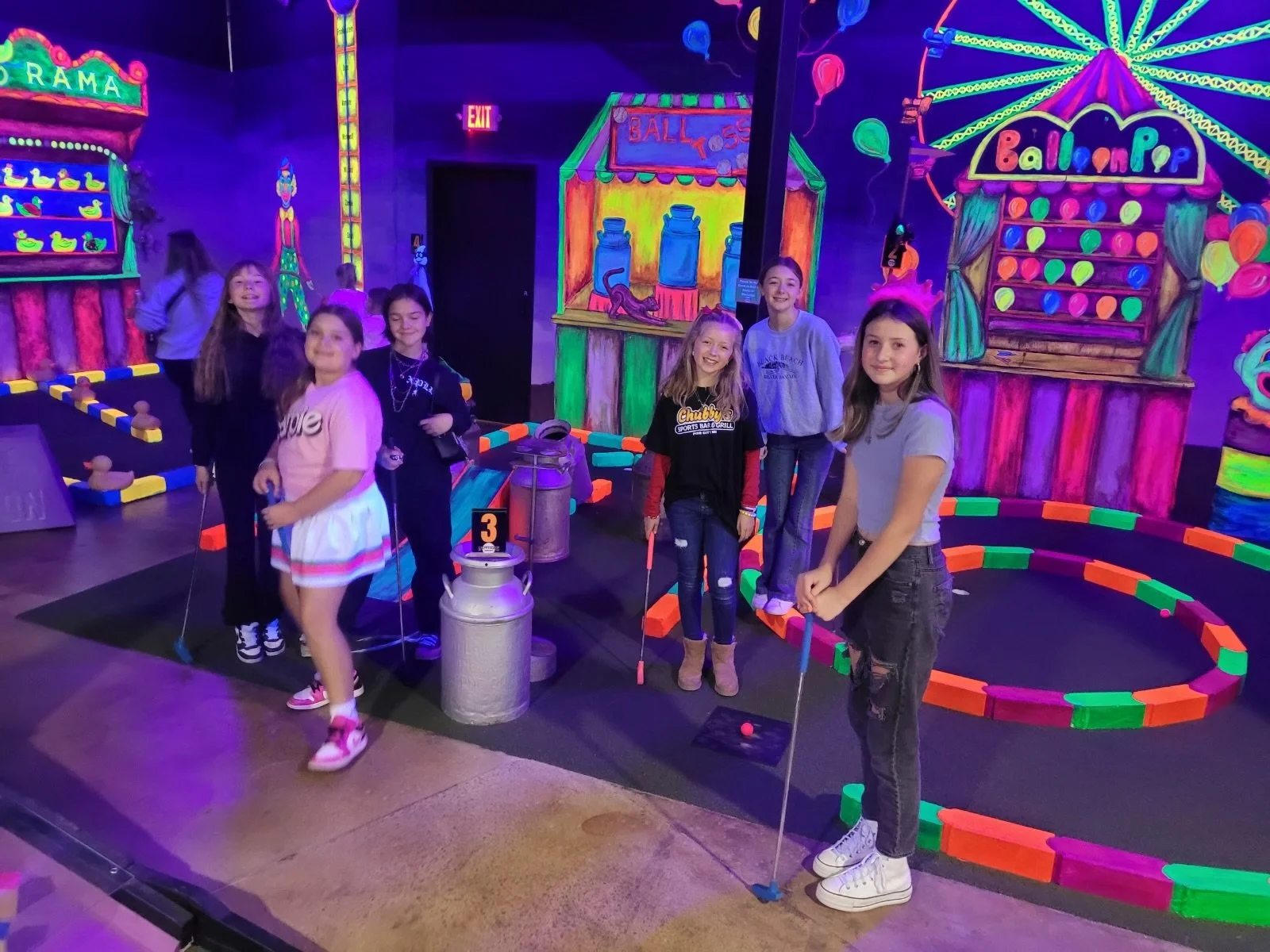 Group of teenage girls playing mini golf on a mini golf course with neon colors and lights surrounding them at Nowhere Entertainment in Inver Grove Heights