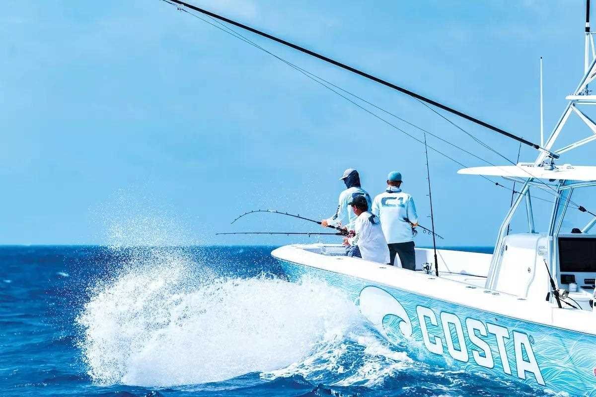 Three men fishing from a boat labeled 'COSTA' on a bright, clear day.
