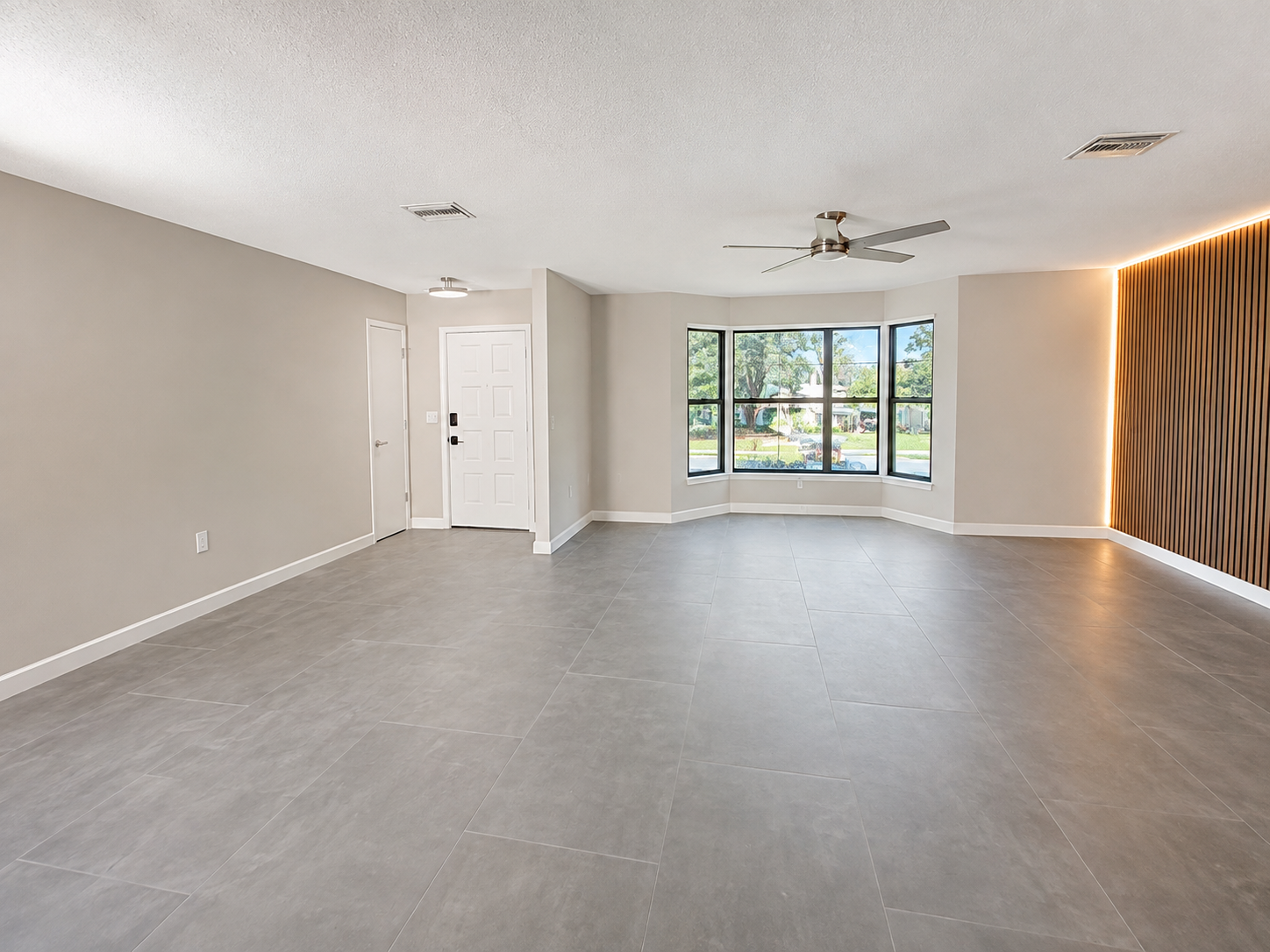 Large living room at the front of the house with bay window and modern wood paneling media wall. 