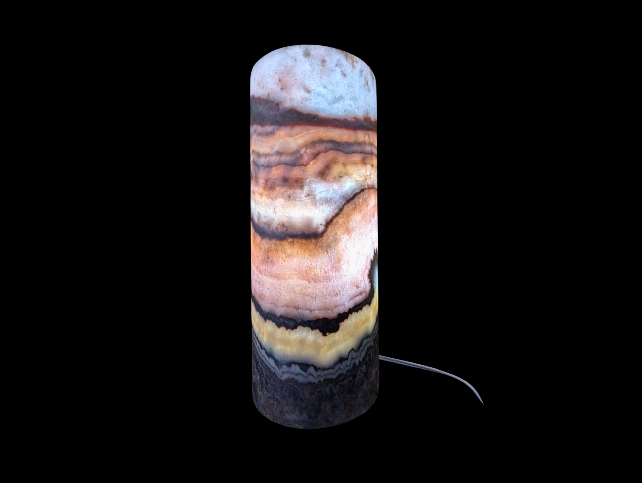 A cylindrical lamp made of banded black and cream onyx stone glowing with warm light on a wooden table