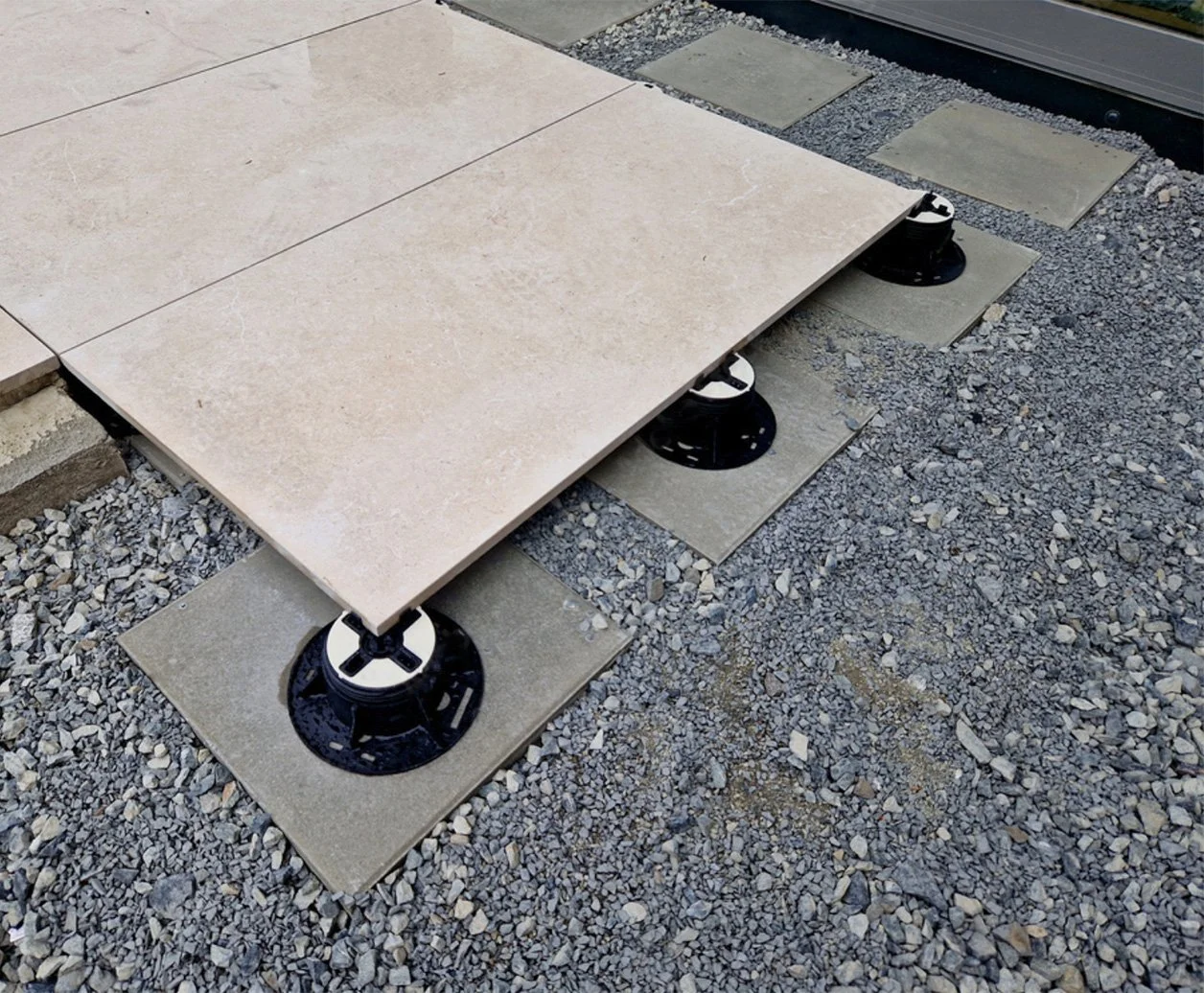 Raised tile decking installed on adjustable pedestal supports over a gravel rooftop surface