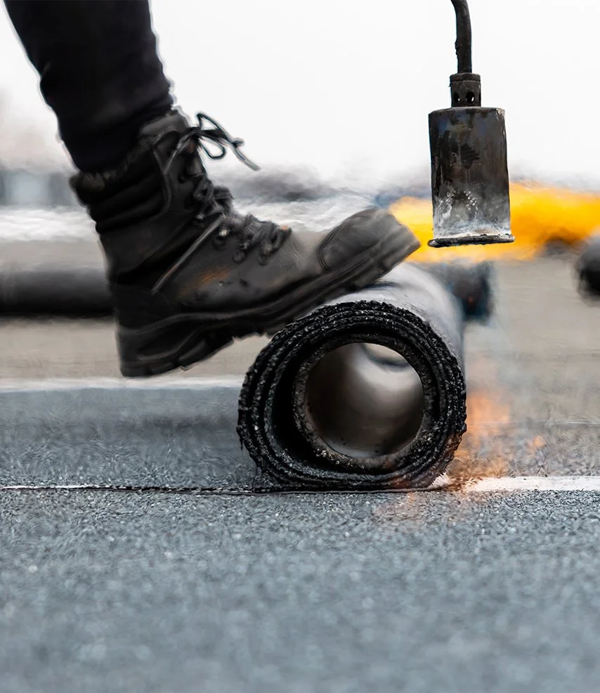 Worker in a black boot stepping on a pipe while welding equipment produces sparks
