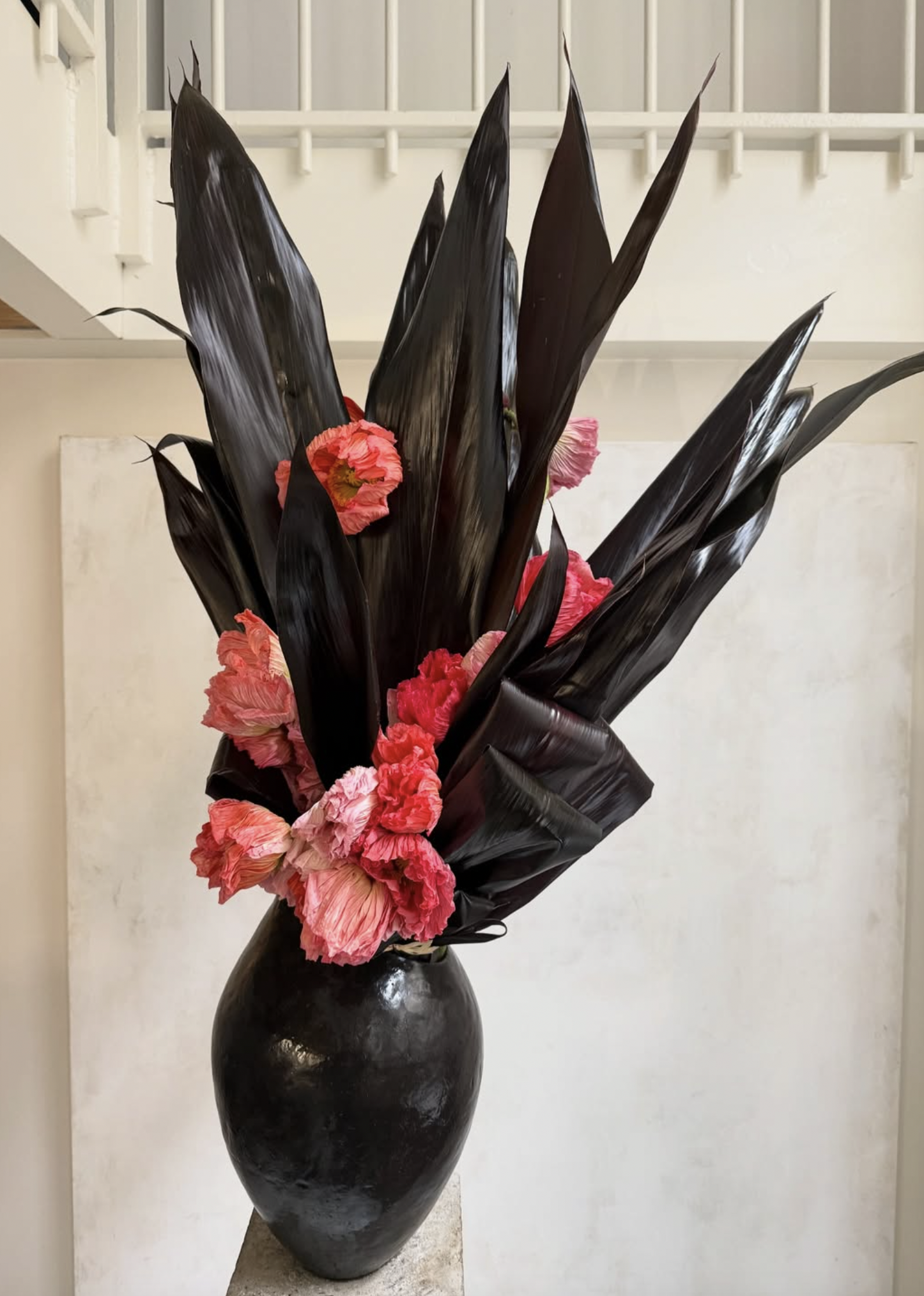 Black vase filled with dark glossy leaves and pink flowers.