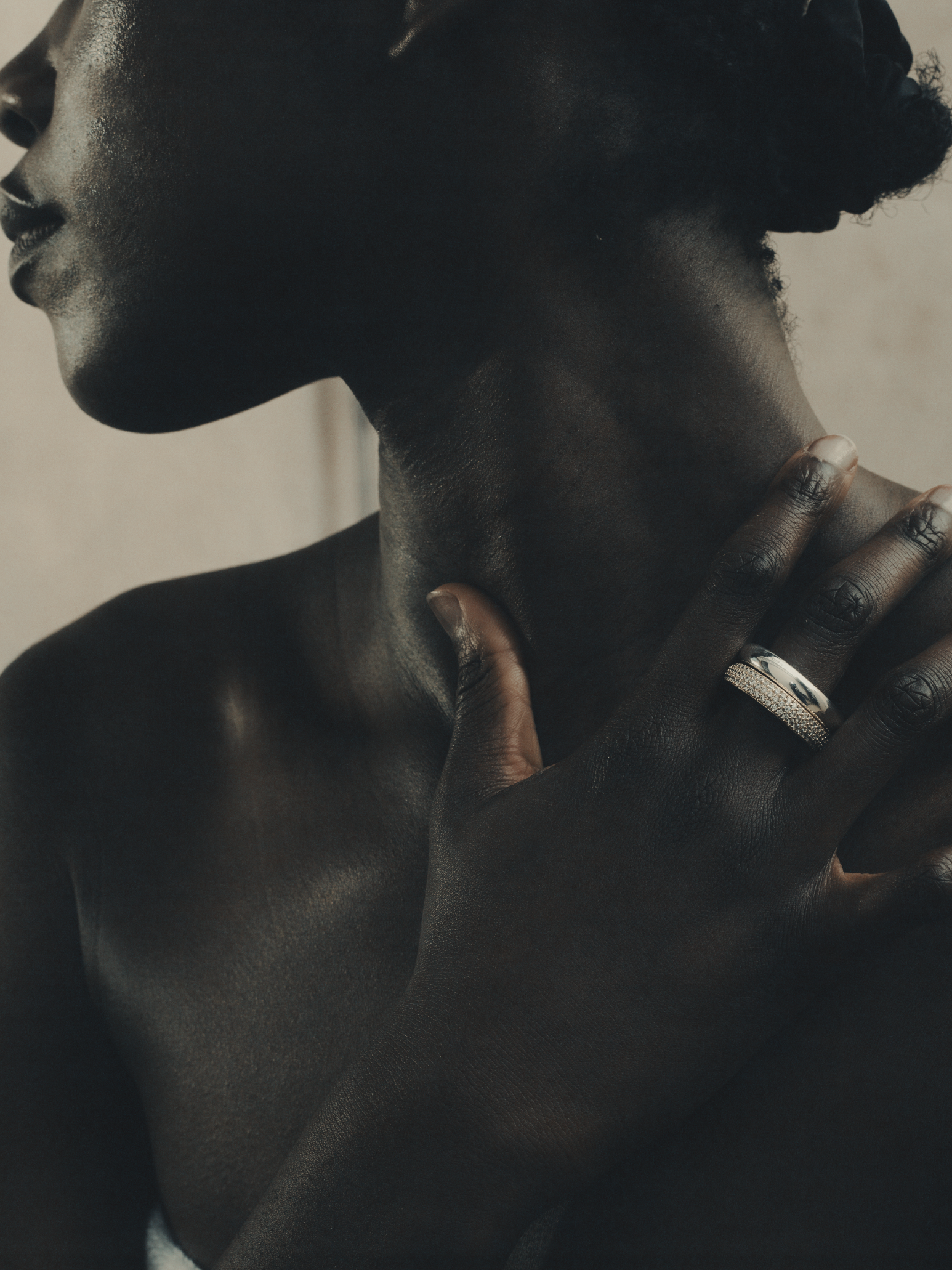 Close-up of a Black person's face and hand touching their neck, with jewelry on the finger.