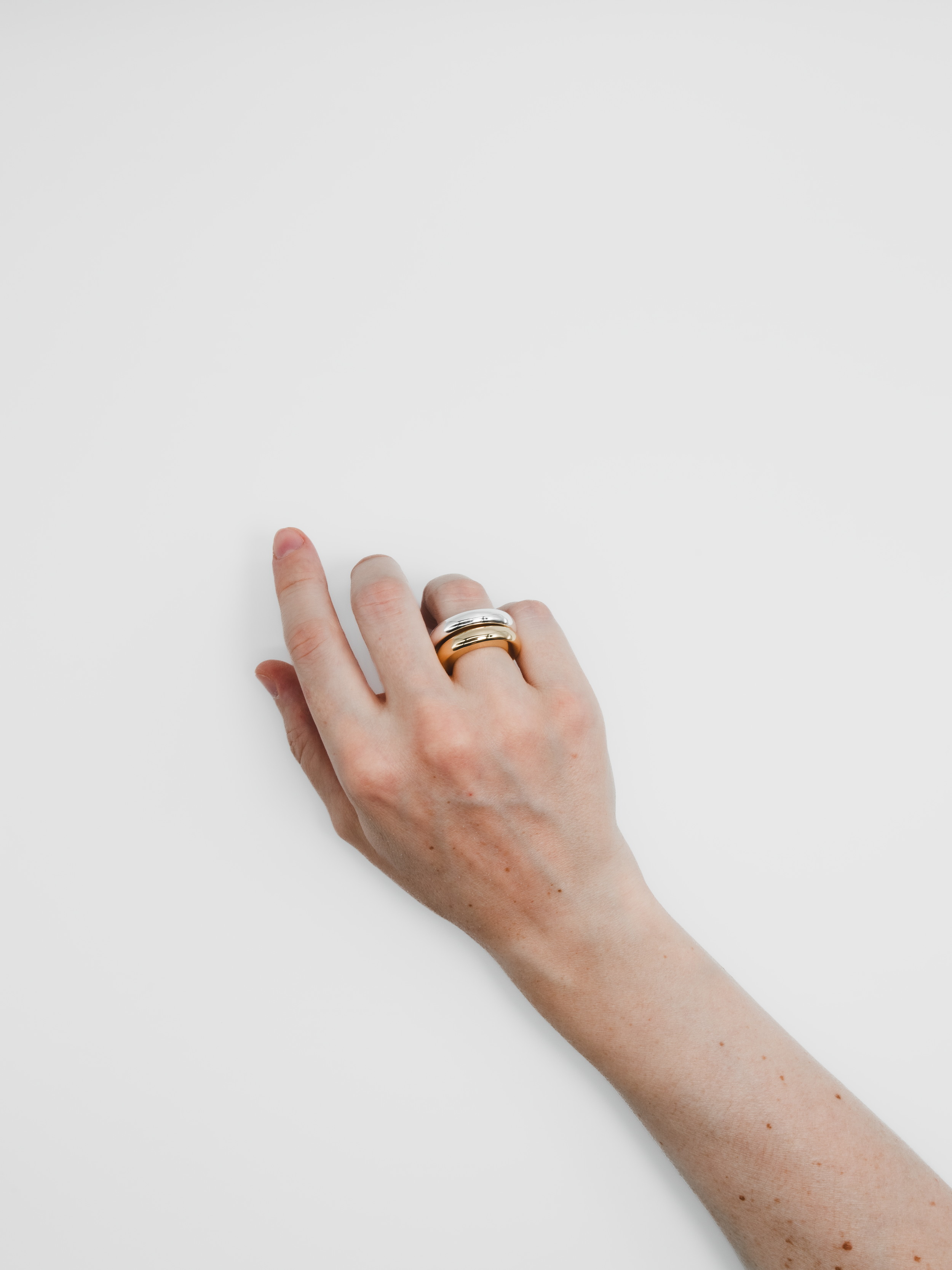 A hand with light skin wearing three rings, resting on a white surface.
