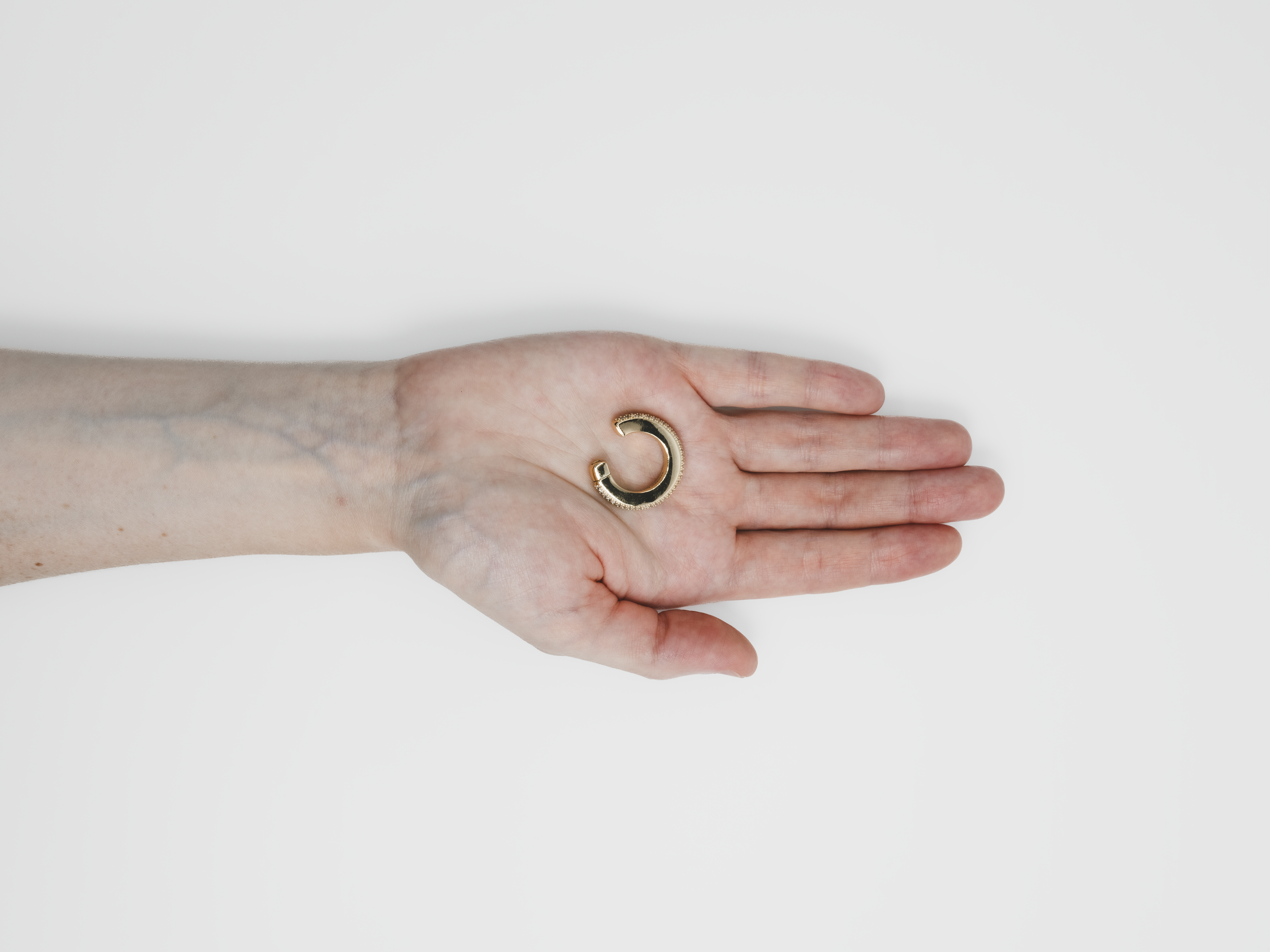 A person's hand with a gold ring resting on a white surface.