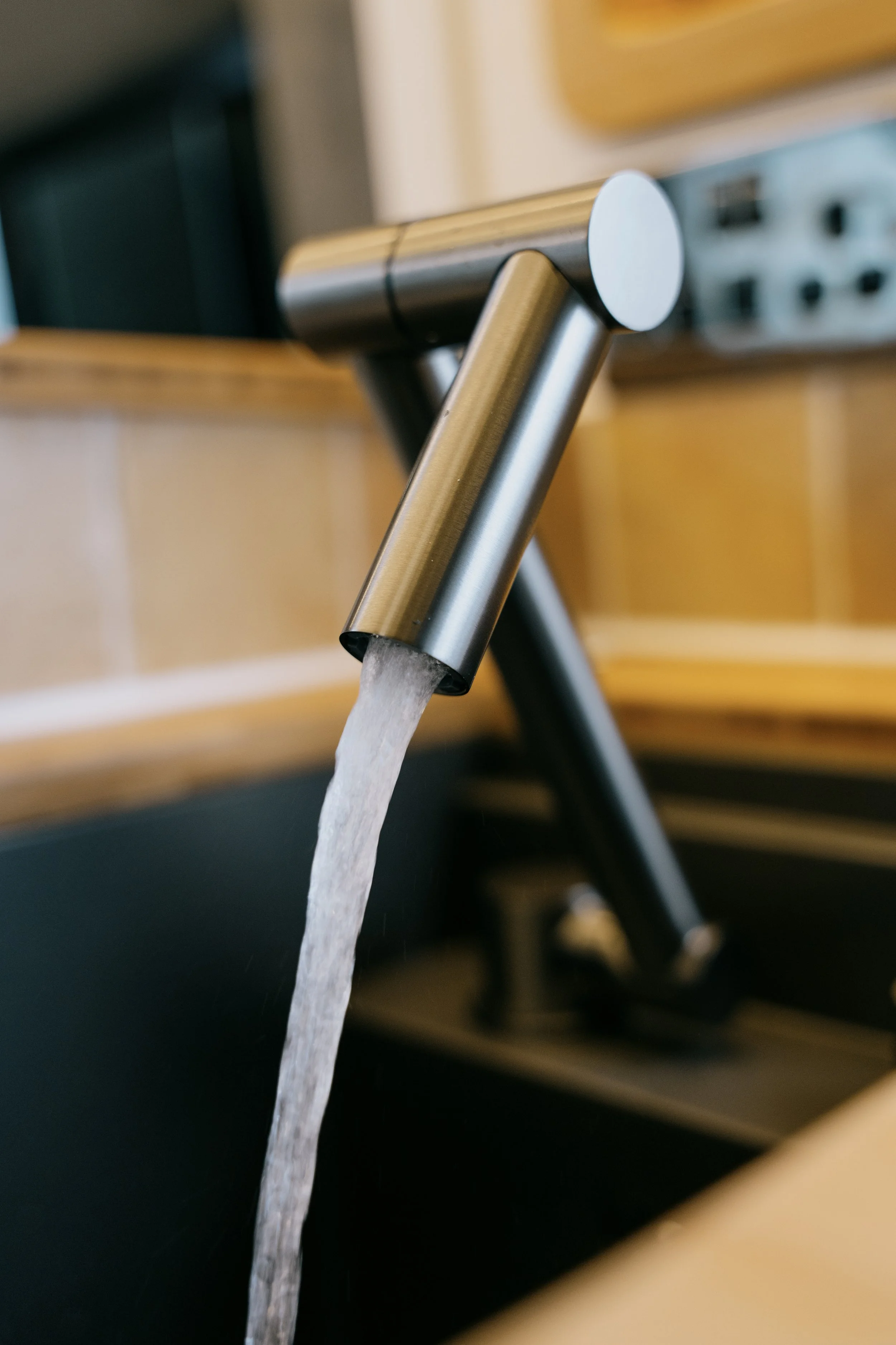 Close-up of a modern stainless steel faucet with running water above a black sink in a kitchen.