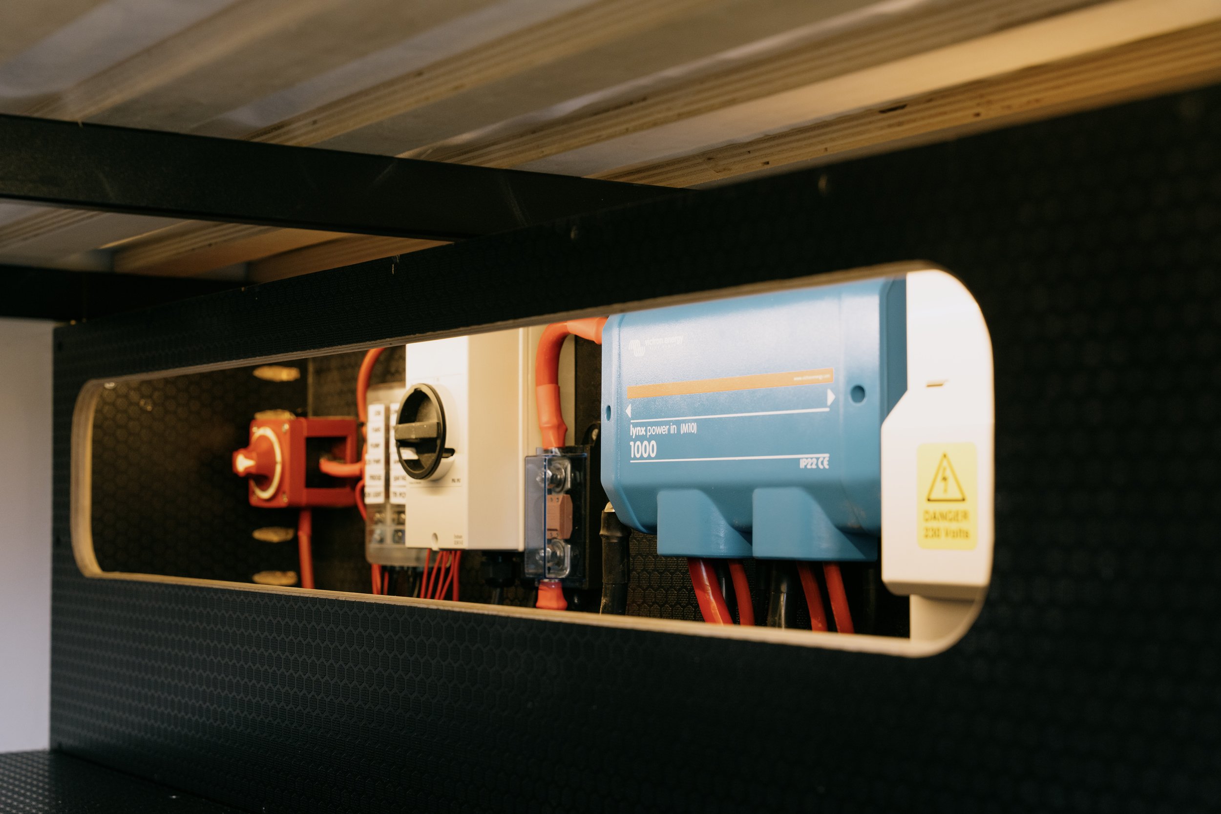 Electrical components inside a black enclosure, including a blue power inverter marked 'lynx power in (M10) 1000' and various red cables, switches, and connectors.