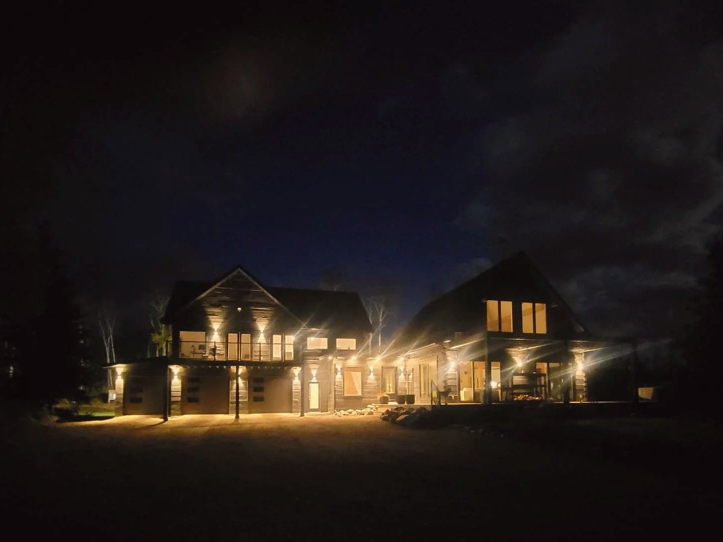 A large house with multiple lit windows and exterior lights at night.