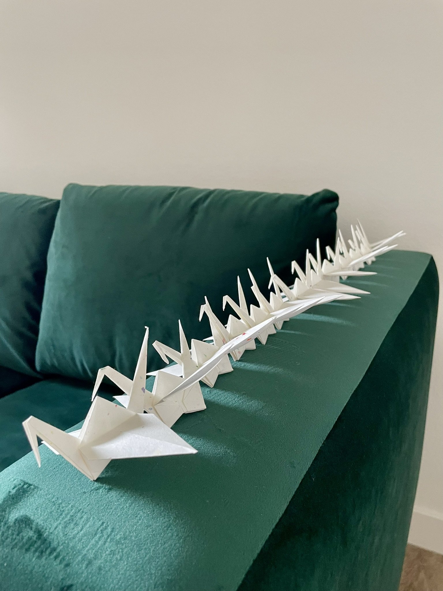 A row of folded paper origami cranes lined up neatly along the arm of a green velvet couch, showcasing intentional home organization philosophy.