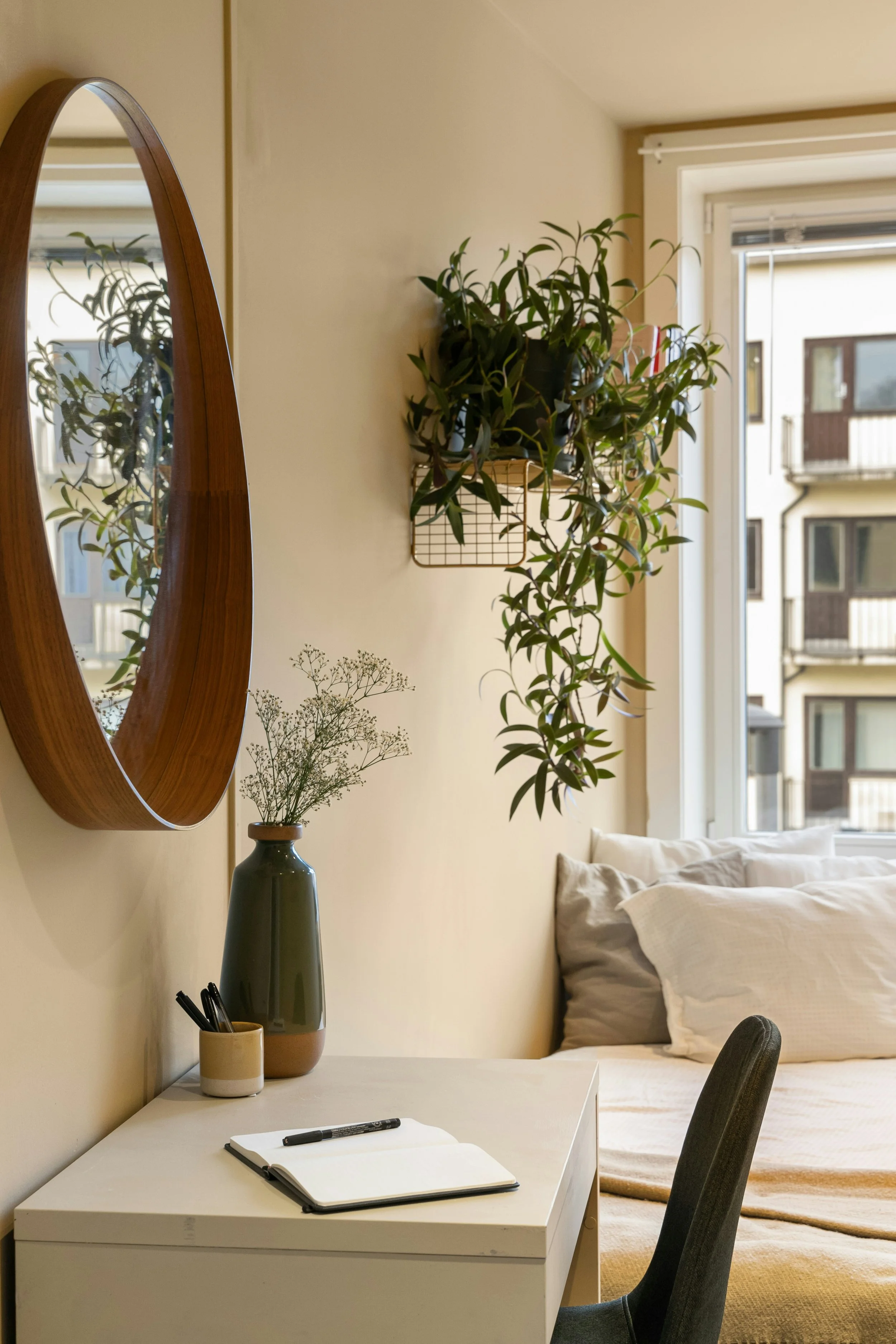 A clean and organized bedroom workspace in Tumwater, Washington, showing a white desk with a notebook, a hanging plant, and a large round wood-framed mirror.