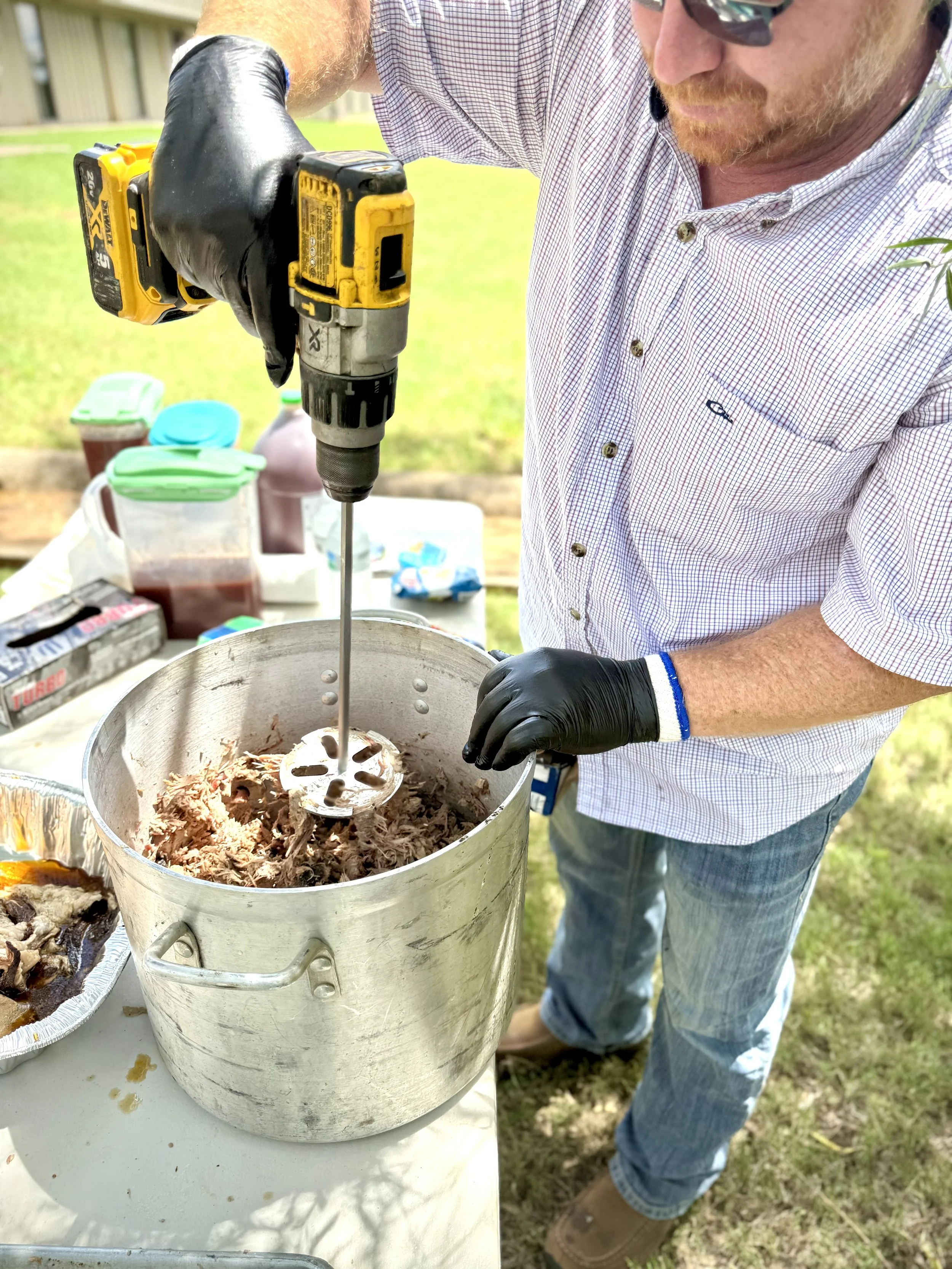 Pulled pork being mixed with BBQ sauce using a drill mixer at Blackwater BBQ to evenly coat meat and preserve texture.