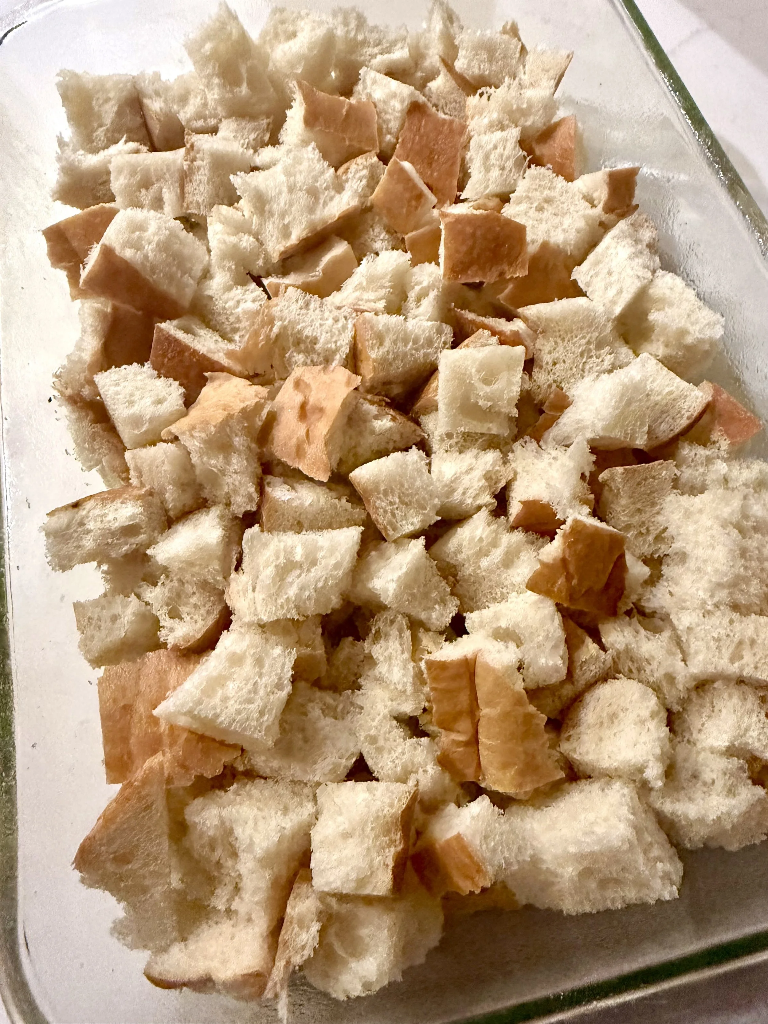 Cubed day old French bread layered in a baking dish for bananas foster bread pudding