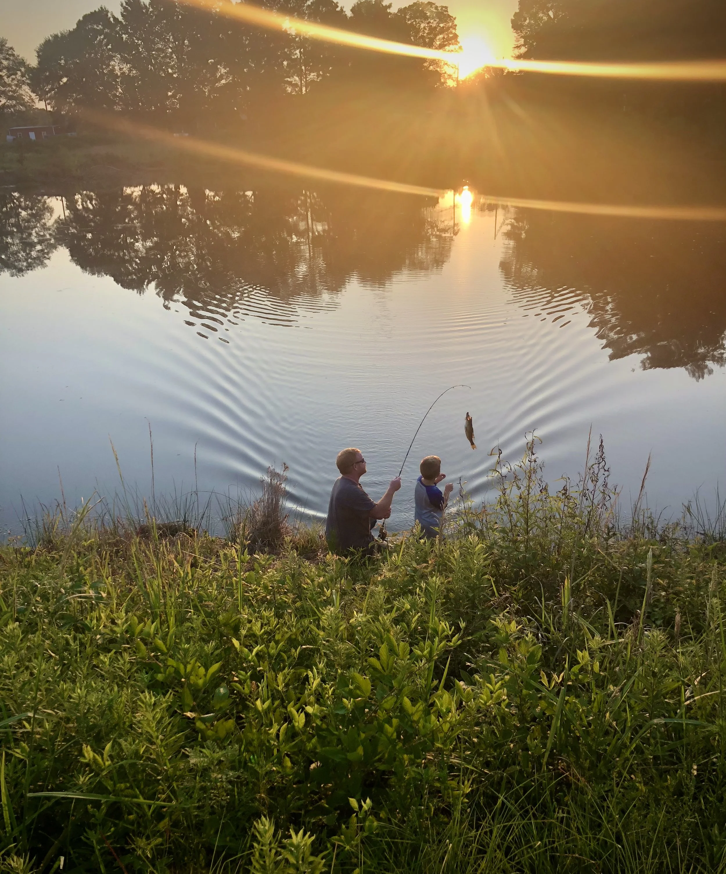 Sunset beautiful light leak with man and boy fishing in a central Alabama pond.