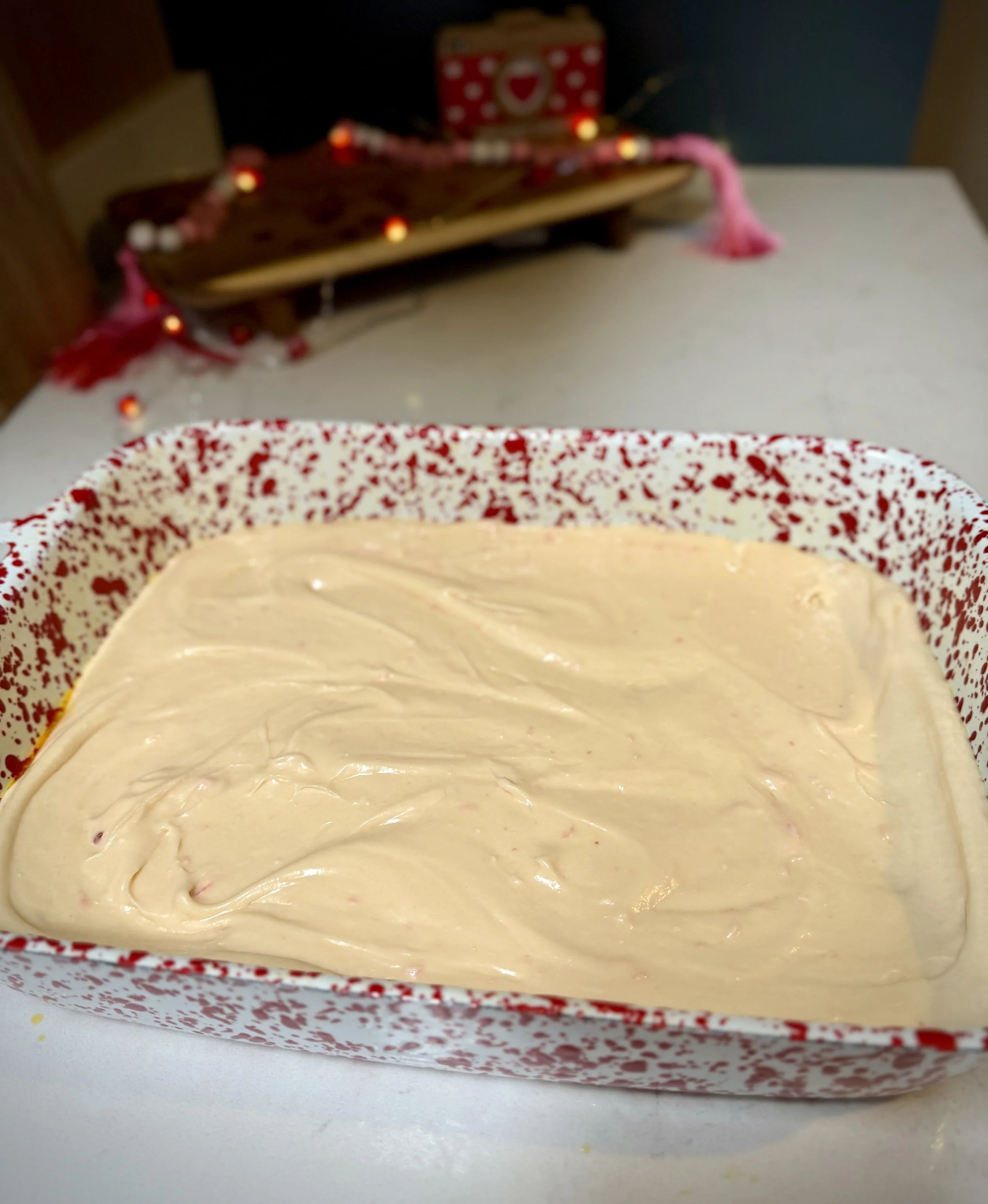 Cream cheese mixture spread over red velvet cake base in a 9X13 speckled baking dish before baking gooey butter cake bars.