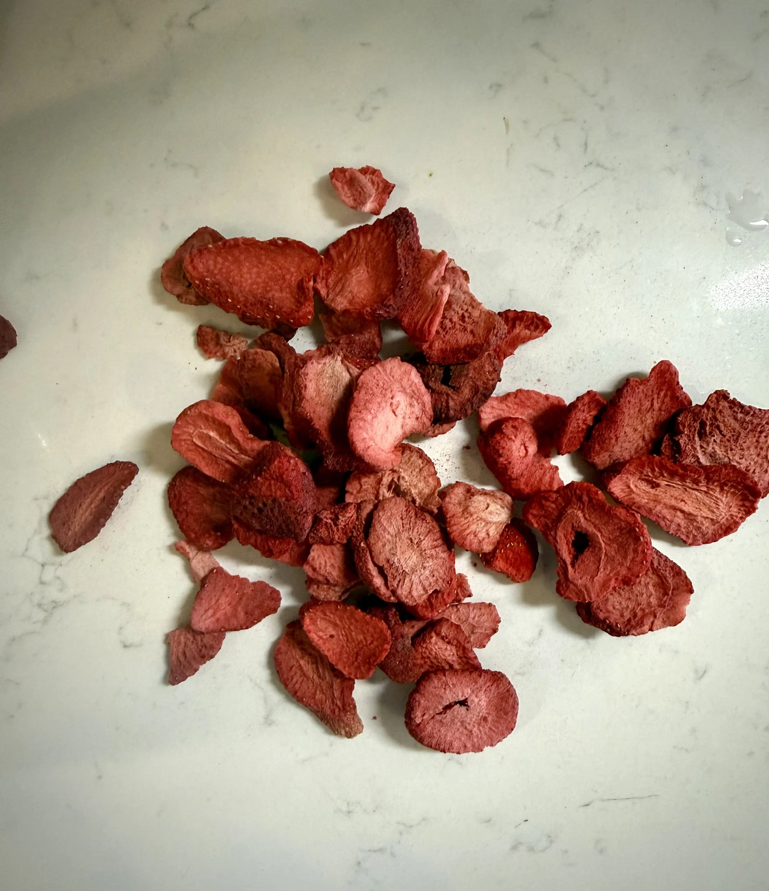 Freeze dried strawberries ready to be crushed on a white Carrara marble countertop.