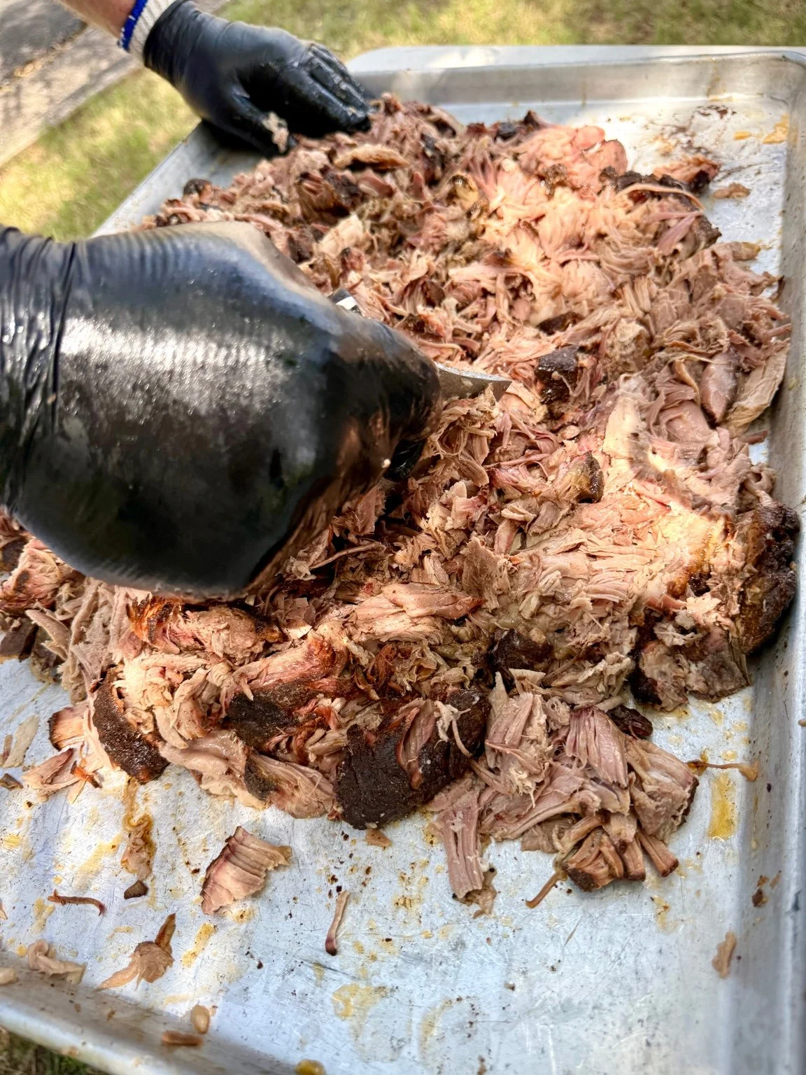 Hnad-pulled smoked pork shoulder being shredded by hand at Backwater BBQ, preserving melt-in-your-mouth bark and texture before saucing.