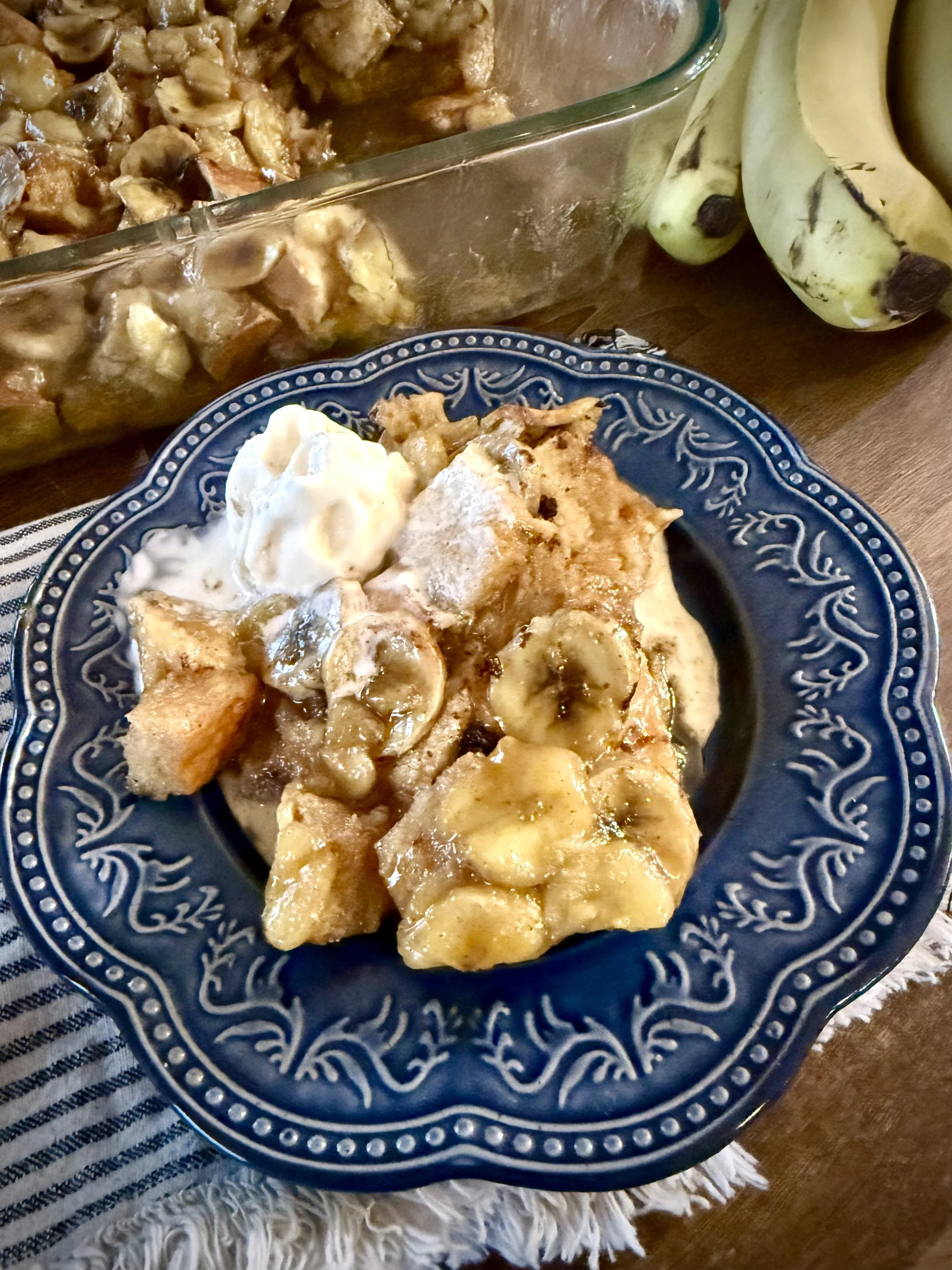 Plated banana fosters bread pudding on a blue lacy plate with bananas and ice cream is a fancy and indulgent cold weather treat!