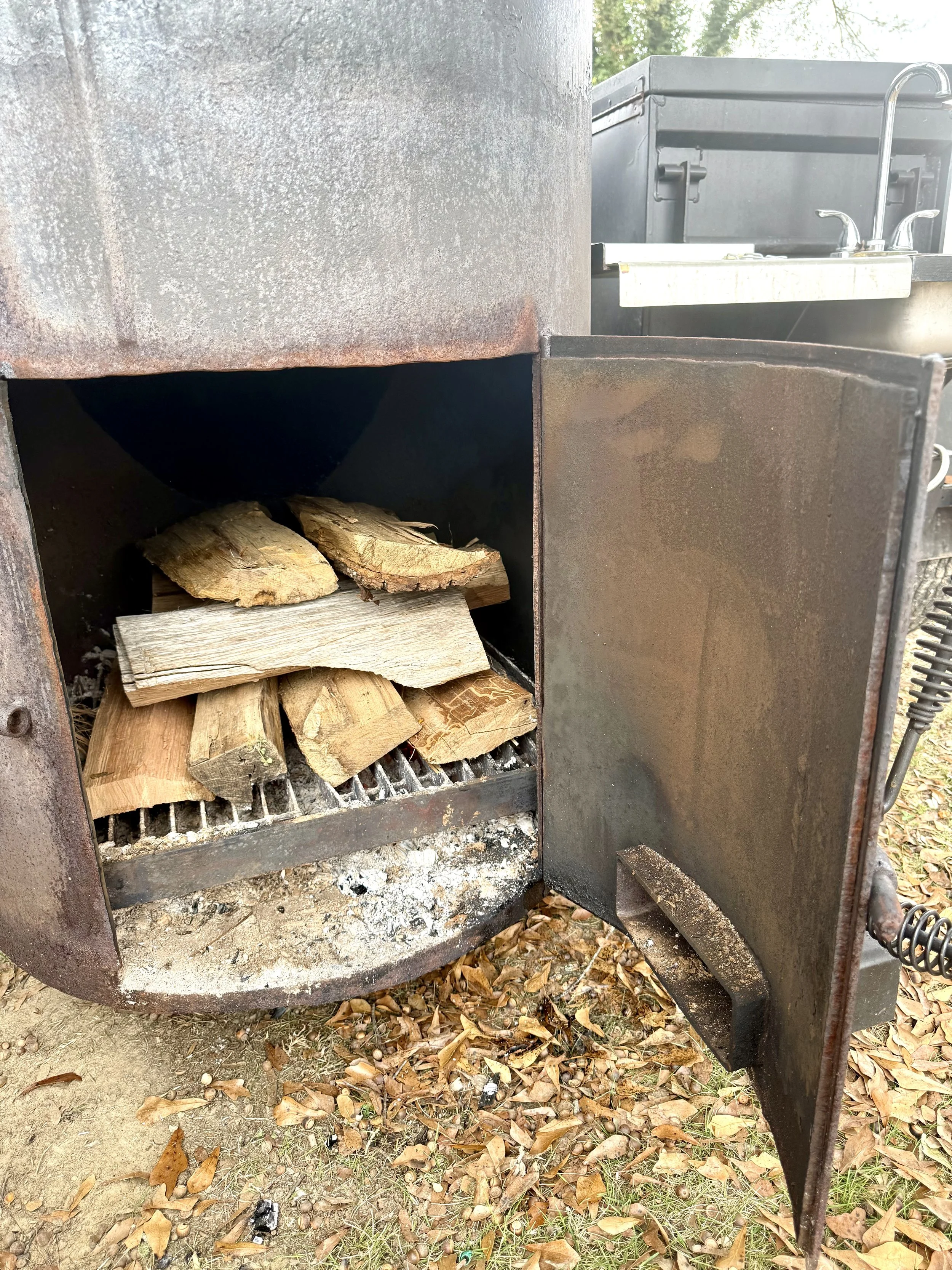 Open firebox on a reverse-flow smoker filled with stackes seasoned hickory and red oak wood, building a steady fire for smoking turkey.