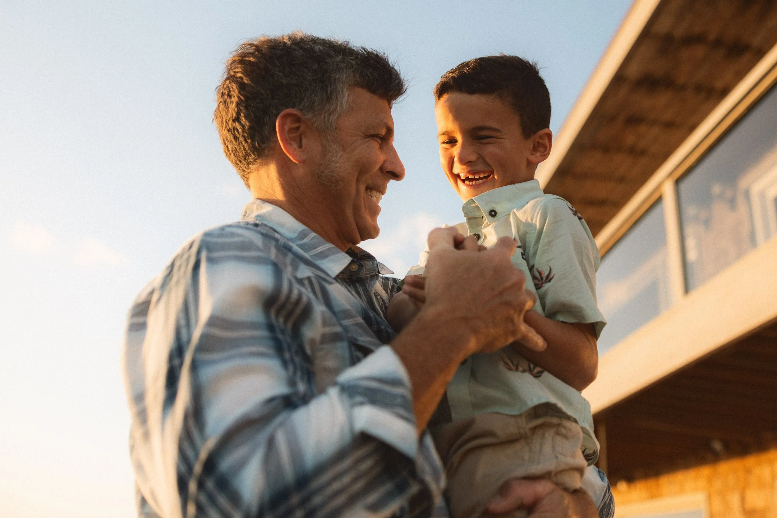 A father laughing while holding his young son during a golden hour family photography session at Capistrano Beach.
