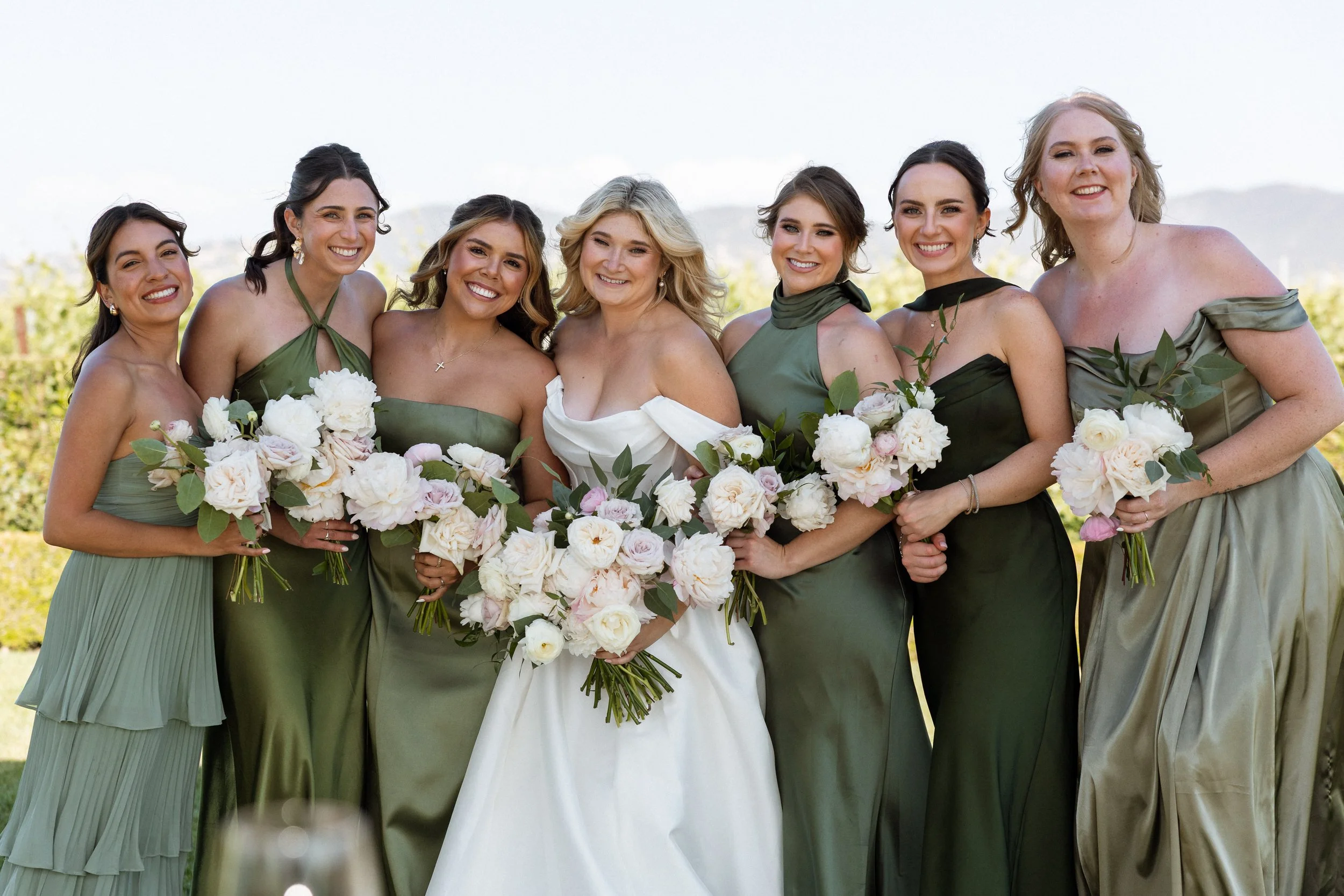 Bride and bridesmaids in sage green dresses with Temecula vineyard hills behind them