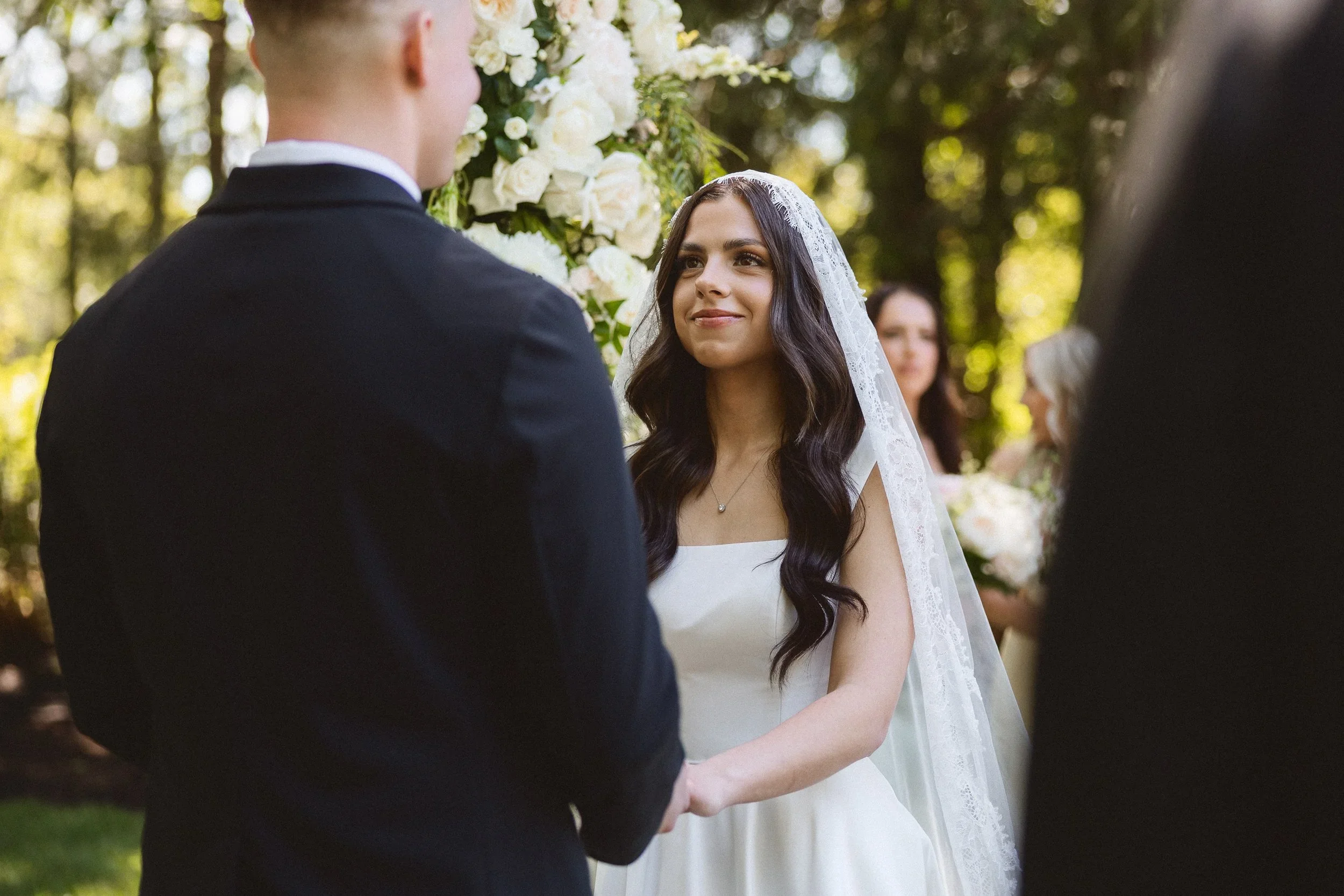 Mark and Angie holding hands and exchanging vows during an intimate outdoor ceremony surrounded by trees at The Hidden Stone Palace.