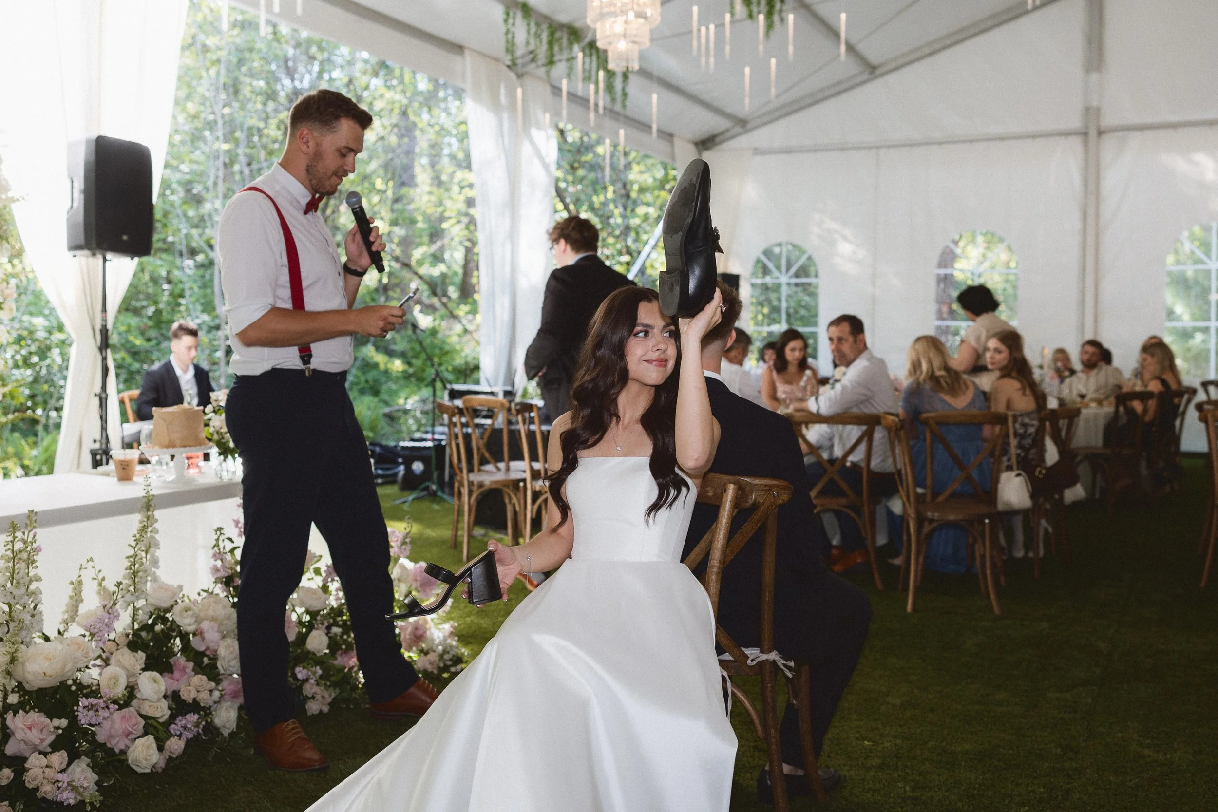 Bride lifts shoe during the wedding shoe game while groom sits behind her