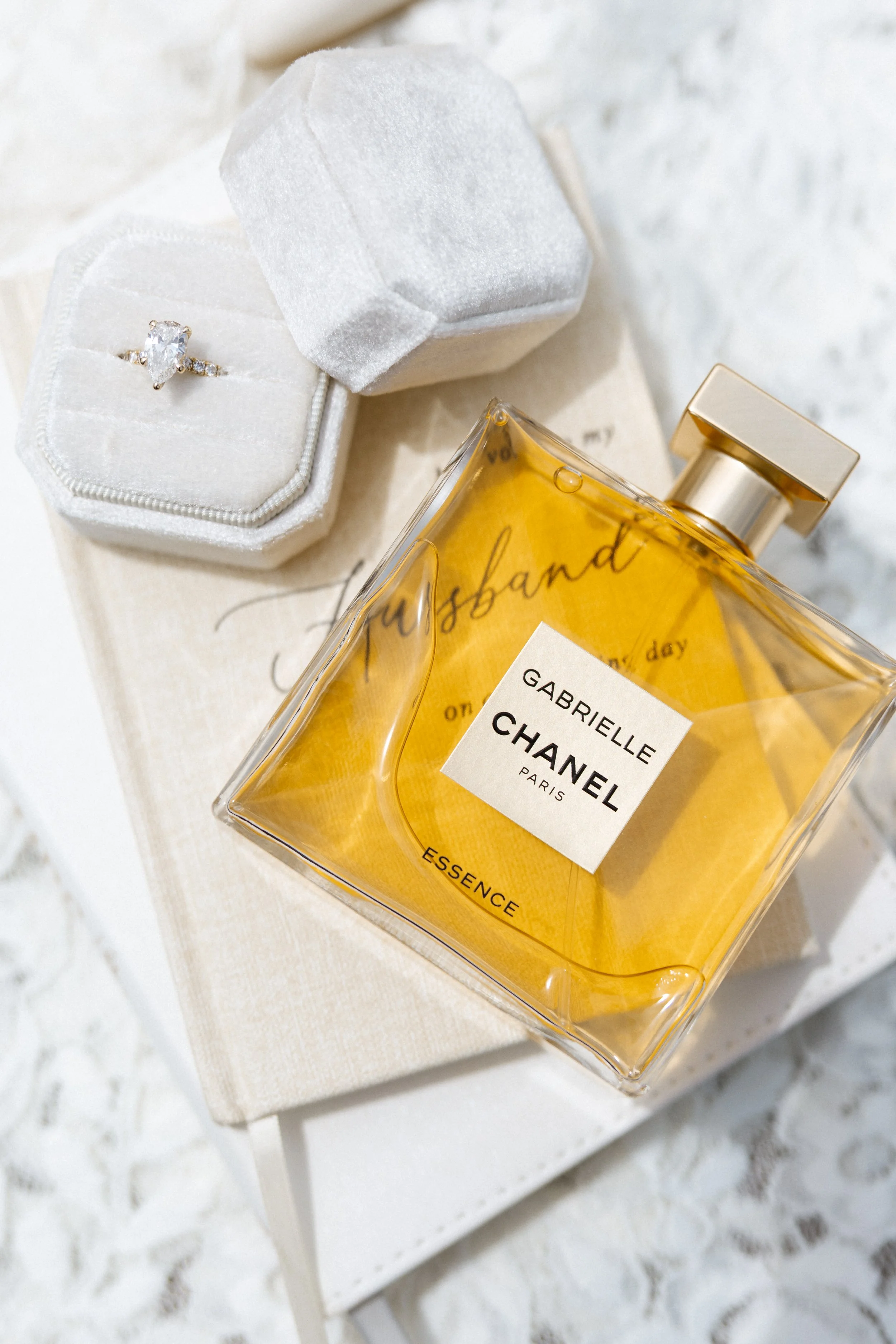 Pear-cut engagement ring in a velvet box beside a chanel perfume bottle and vow card