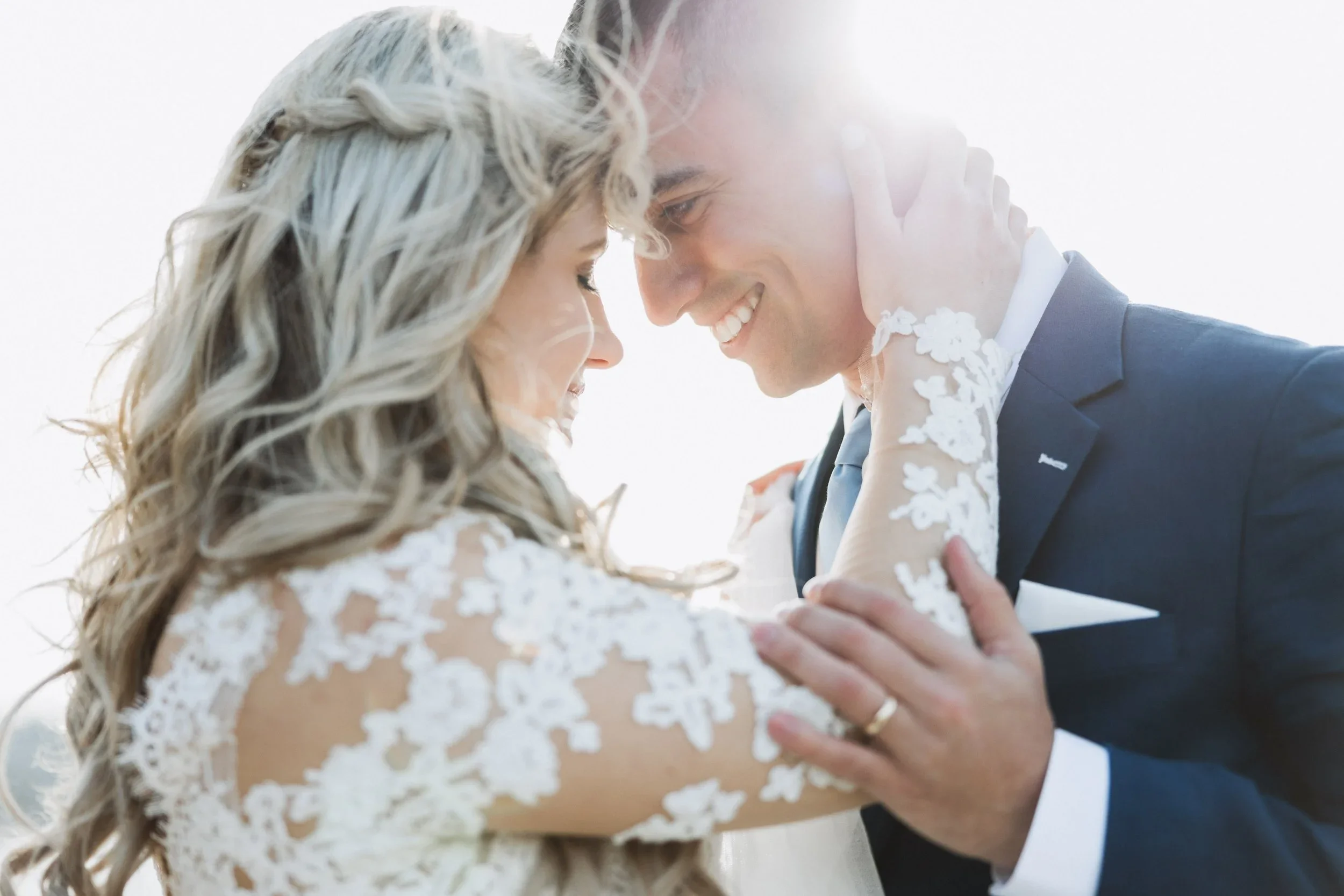 A romantic, sunlit close-up of a bride and groom touching foreheads and smiling during their wedding celebration at the Ukrainian Baptist Church.
