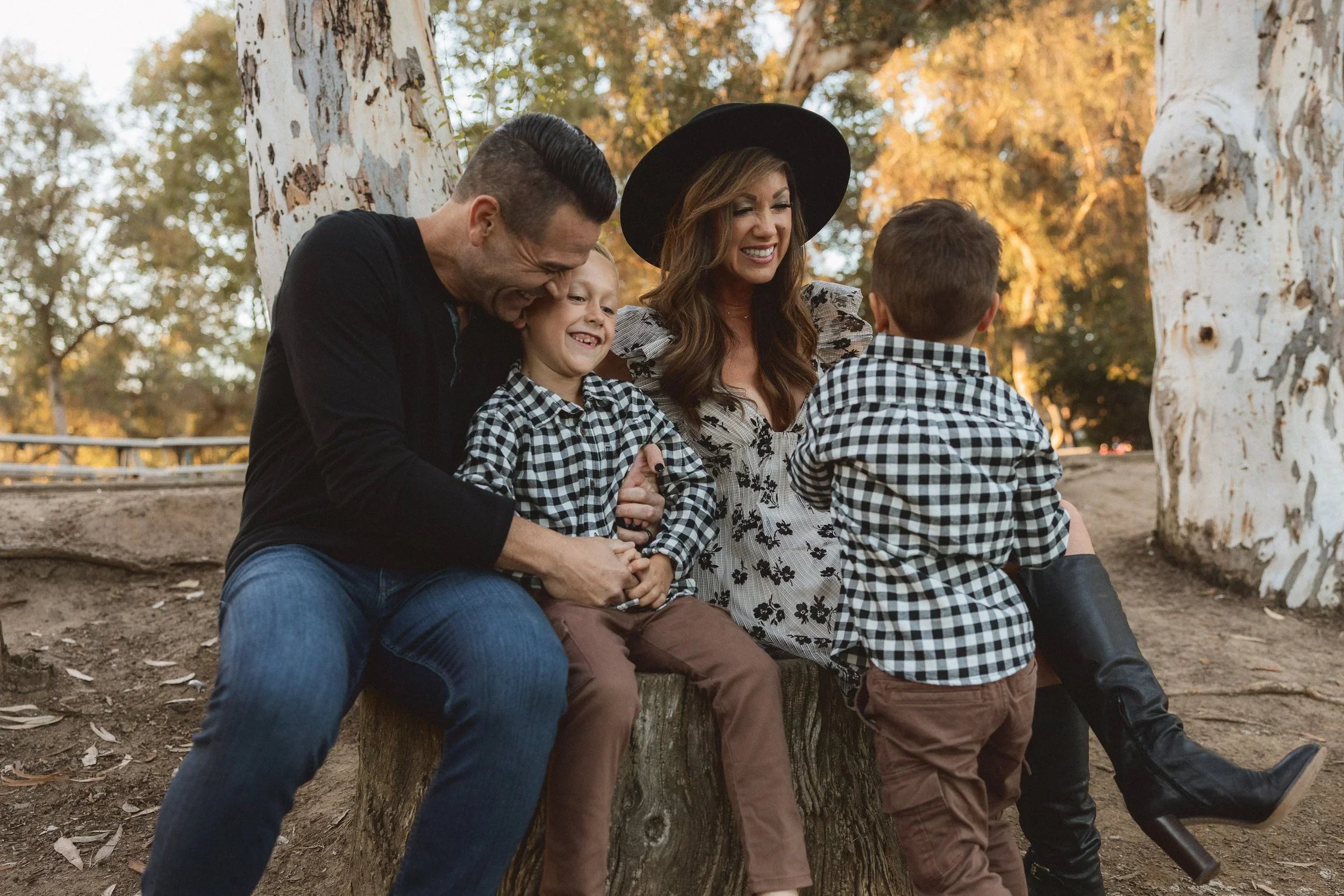 A family of four sitting together on a large wooden log under eucalyptus trees at Turtle Rock Community Park in Irvine.