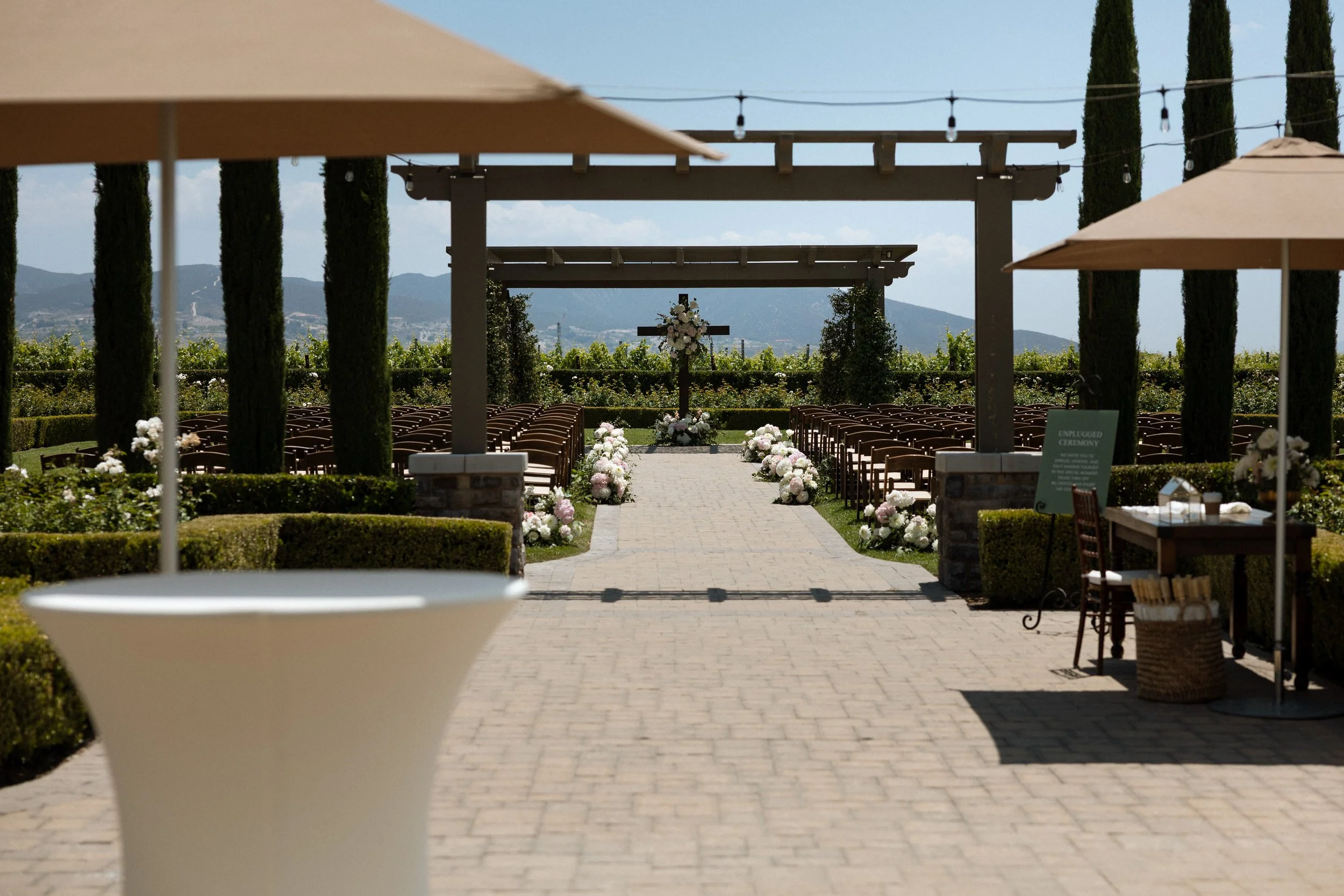 Outdoor ceremony aisle with floral-draped cross and vineyard and mountain views