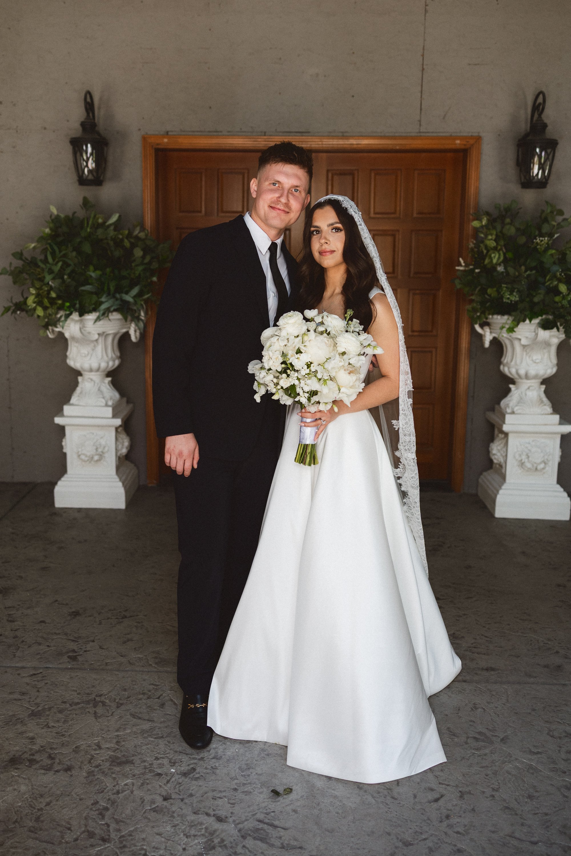 Bride and groom pose in front of wooden doors holding bouquet