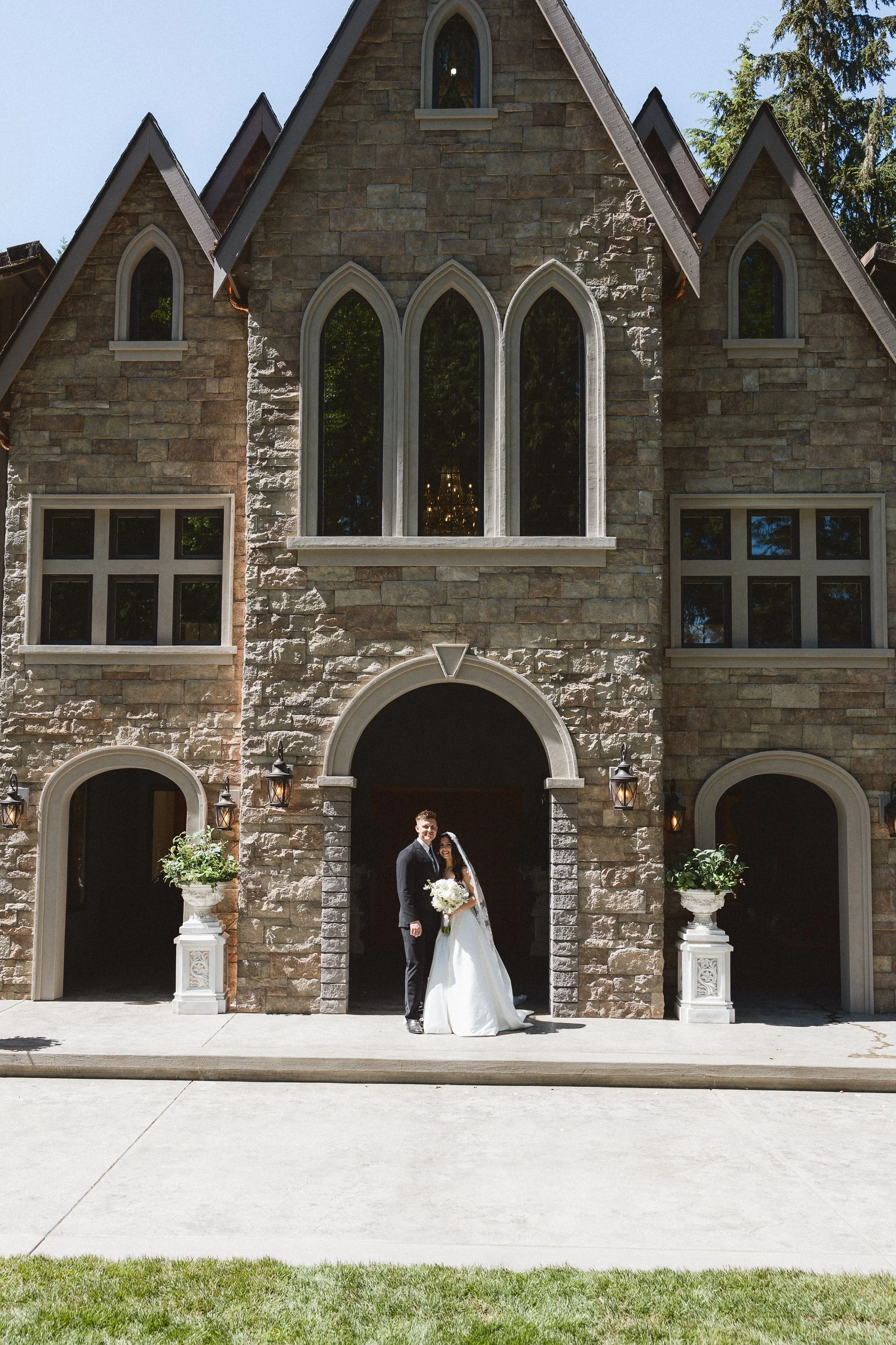 Bride and groom stand in front of stone chapel facade
