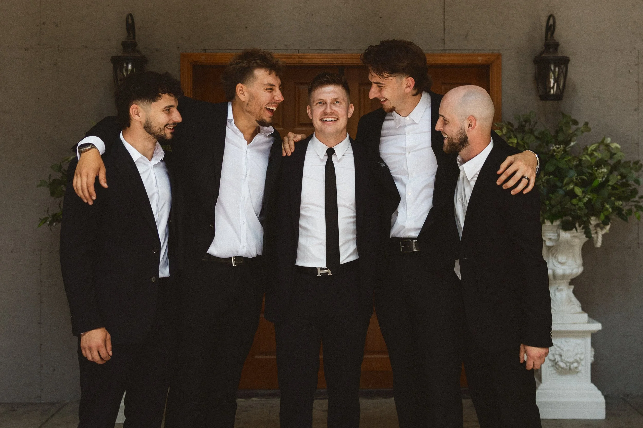Groom sharing a laugh and group hug with his groomsmen outside the venue.