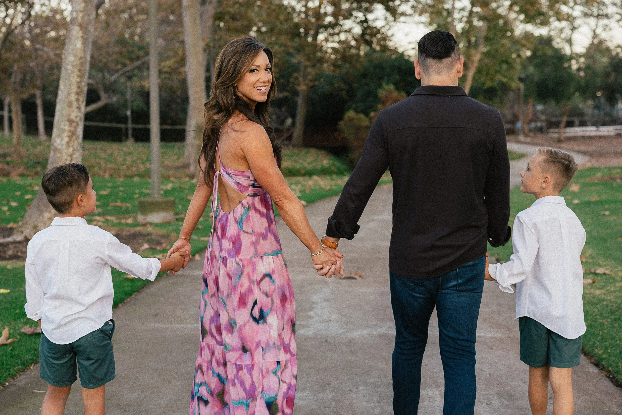 Family holding hands and walking down a path, with the mom turning back and smiling.