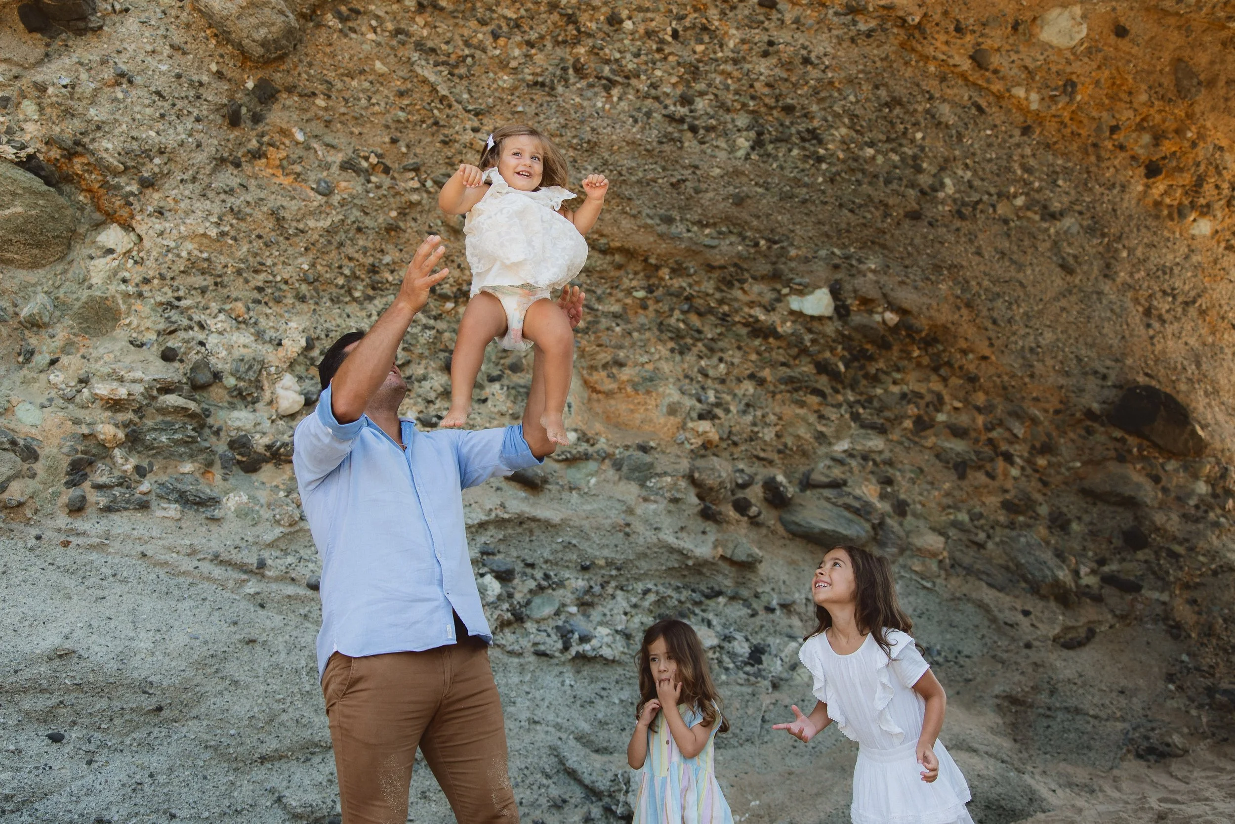 Father playfully tosses daughter in air as siblings cheer during photo shoot.