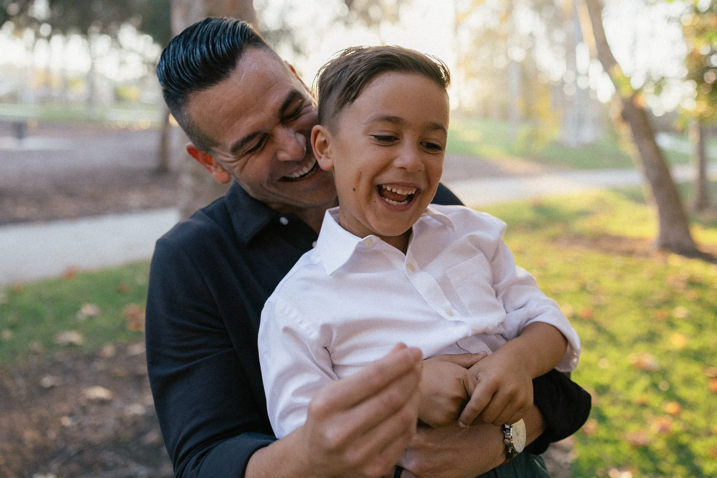 A candid, joyful moment of a father laughing while holding his young son in his arms at Turtle Rock Community Park.