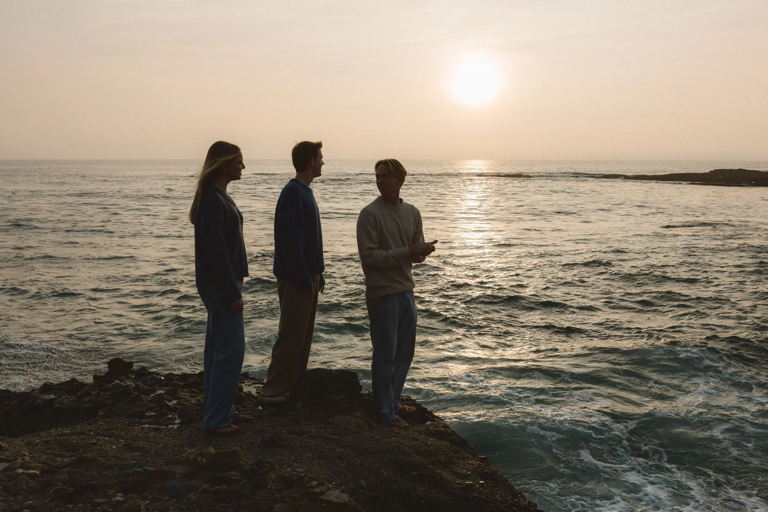 Three siblings standing on a rocky cliff overlooking the ocean at sunset during a golden hour session at Treasure Island Beach in Laguna.