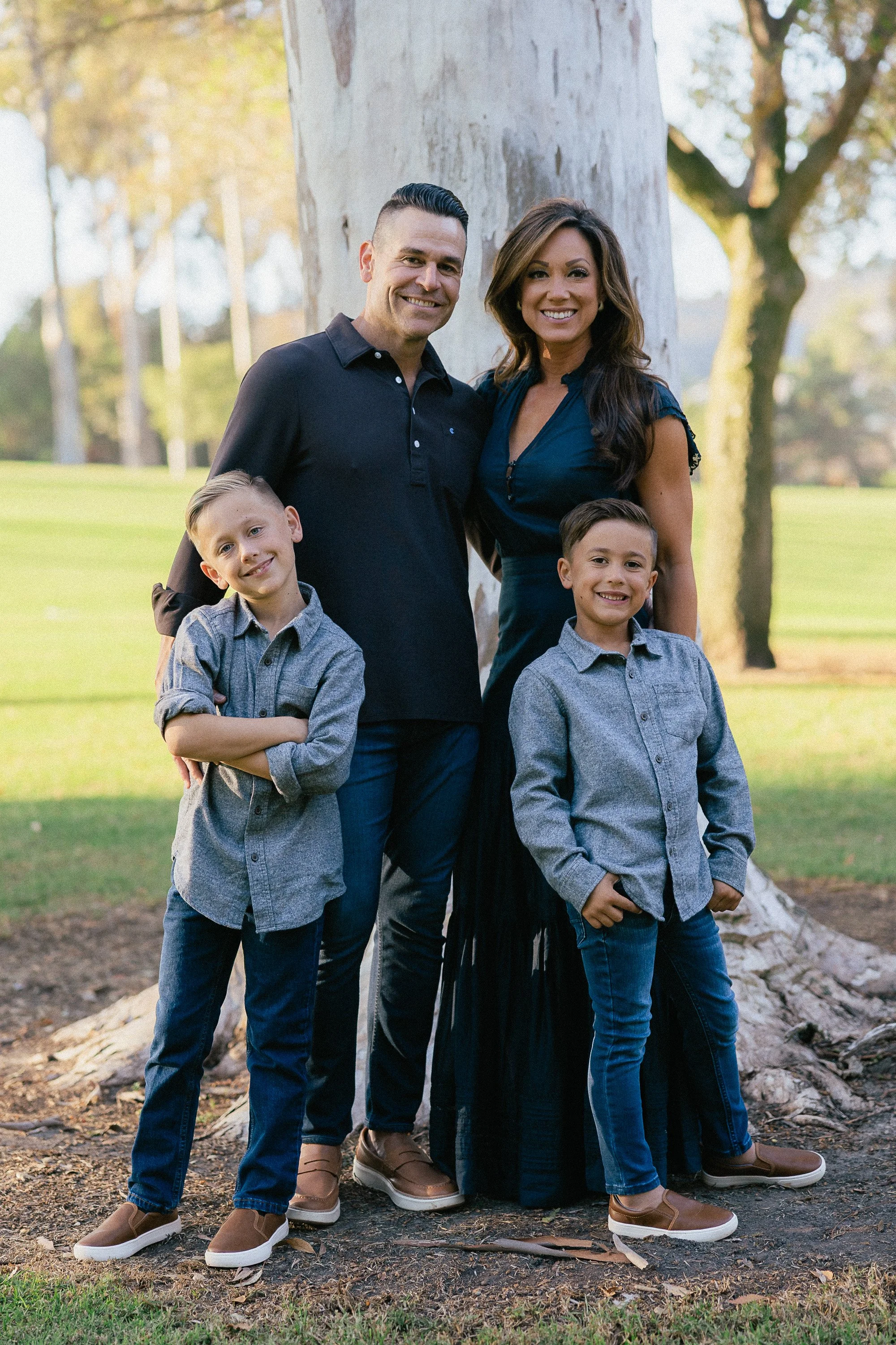 amily portrait standing together in front of a large tree with warm afternoon light.