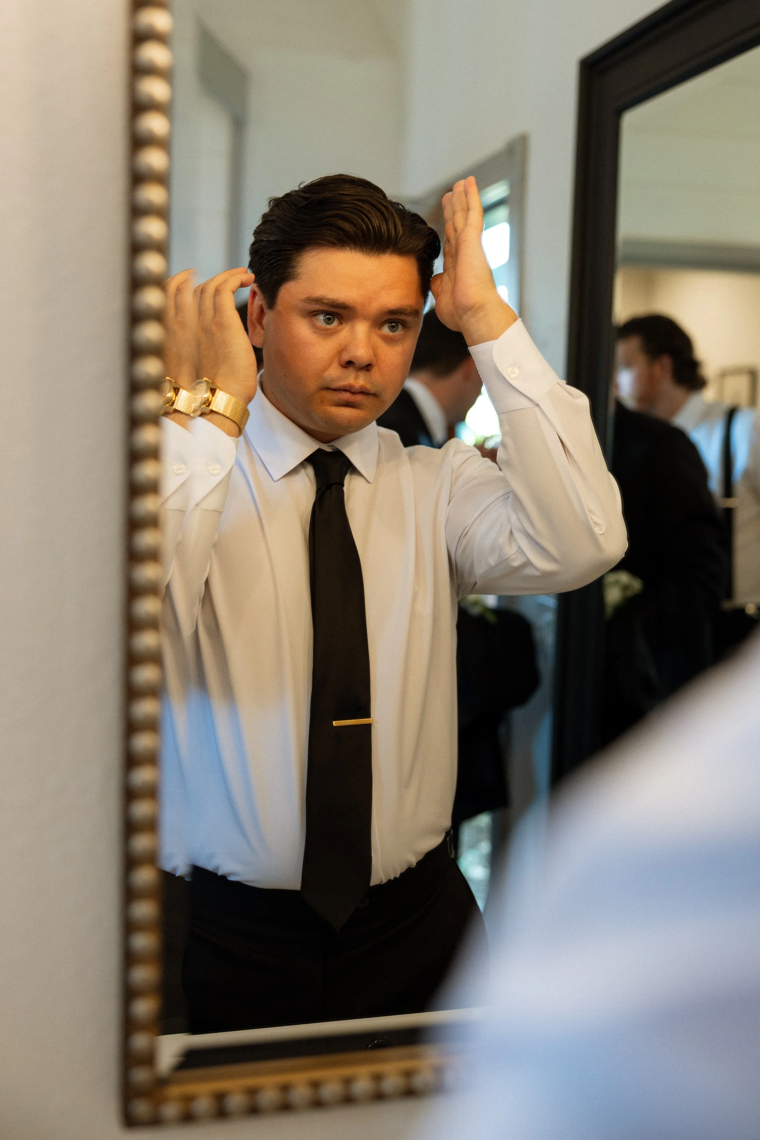 Groom checks his hair in a gold-framed mirror while getting ready