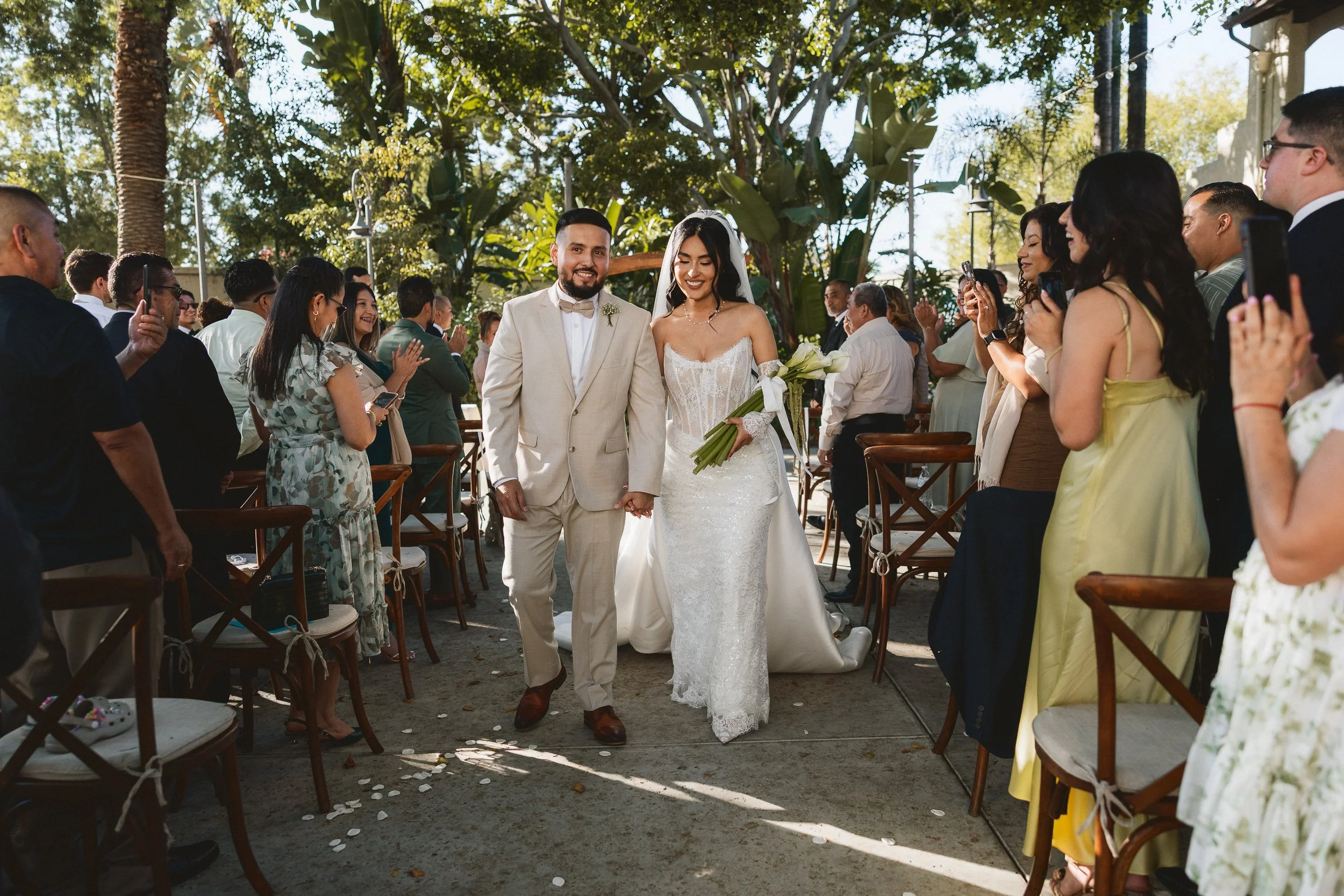 Bride and groom walking down the aisle together as guests applaud at Los Angeles River Center and Gardens.