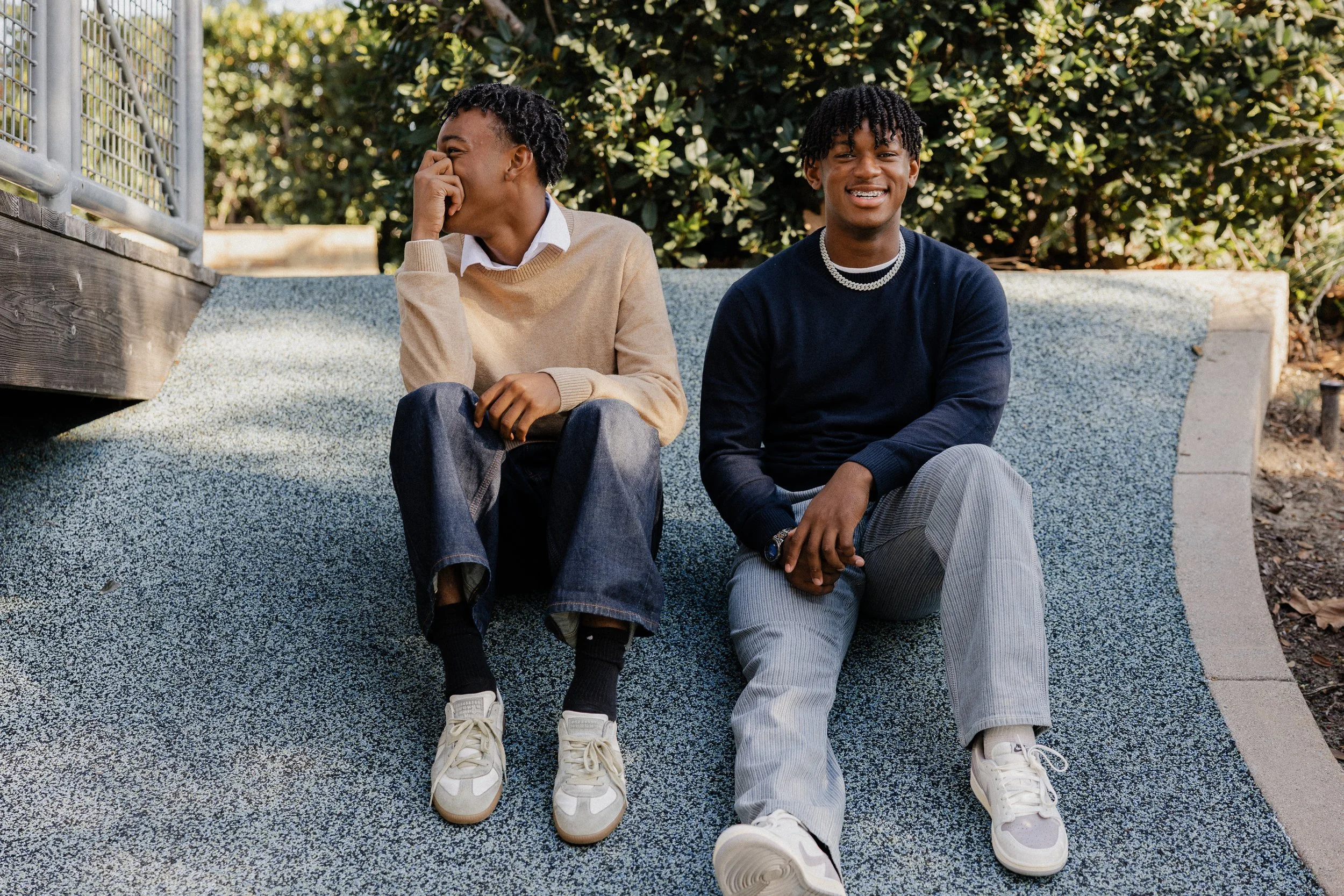 Two teenage brothers laughing and sitting on the blue ground during a candid holiday photoshoot in Irvine.
