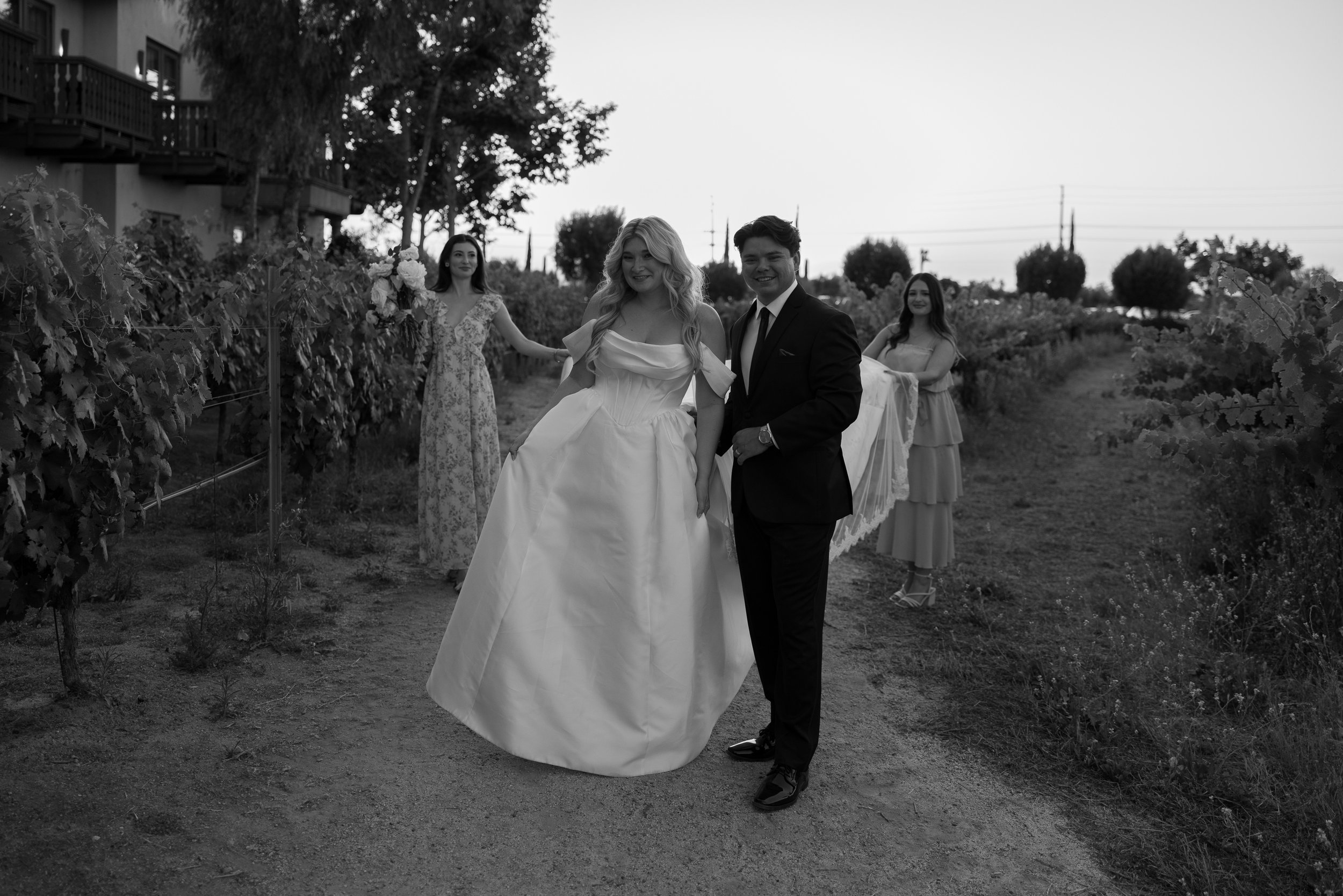 Bride and groom pose in the vineyard with bridesmaids behind in black and white