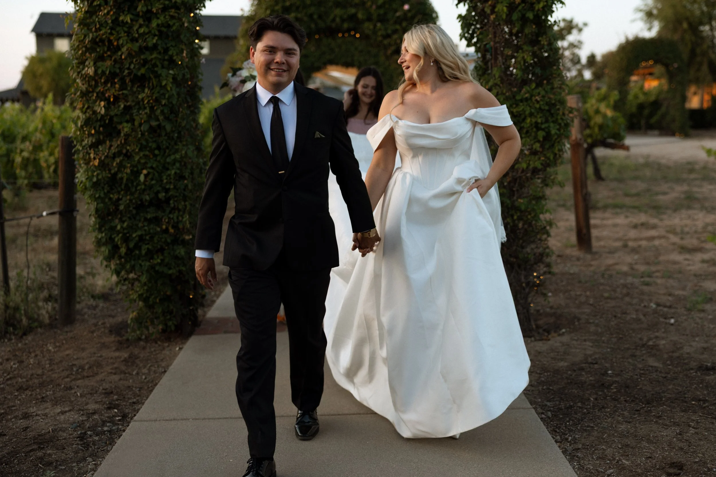 Bride and groom walk hand in hand along a garden path at dusk