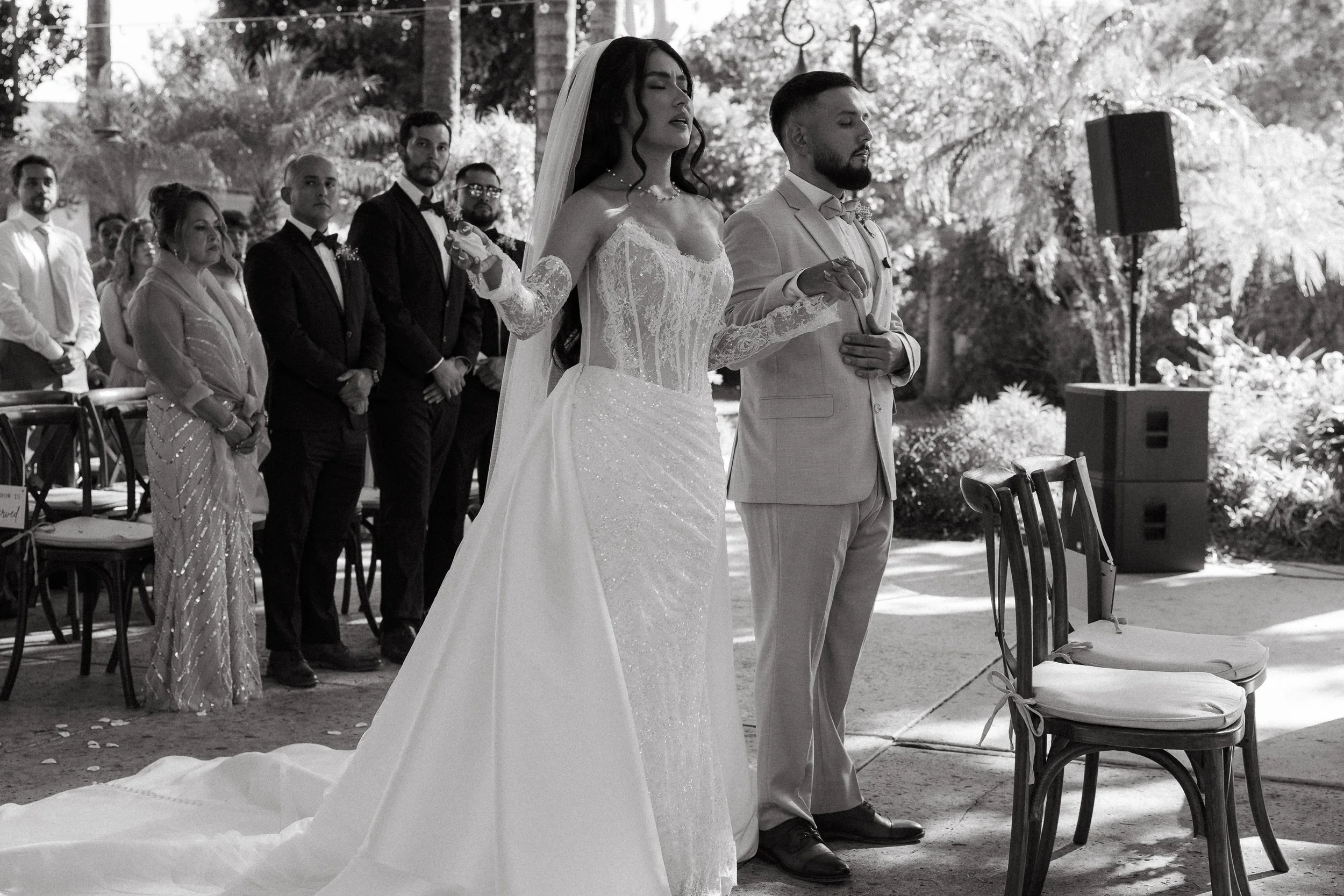 Bride and groom holding hands in prayer during their outdoor wedding ceremony at Los Angeles River Center and Gardens.