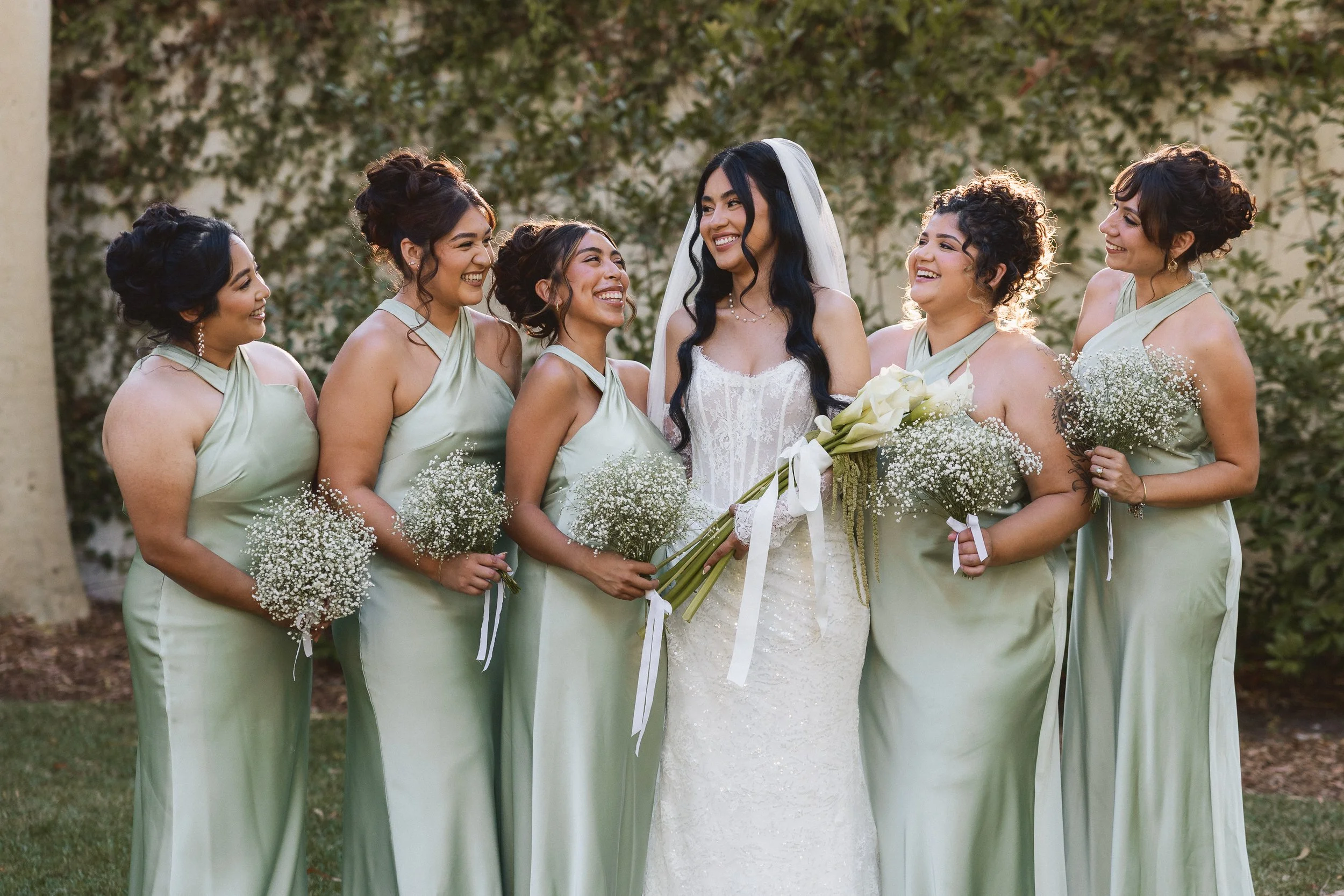 Bride laughing with bridesmaids in sage green dresses at Los Angeles River Center and Gardens.