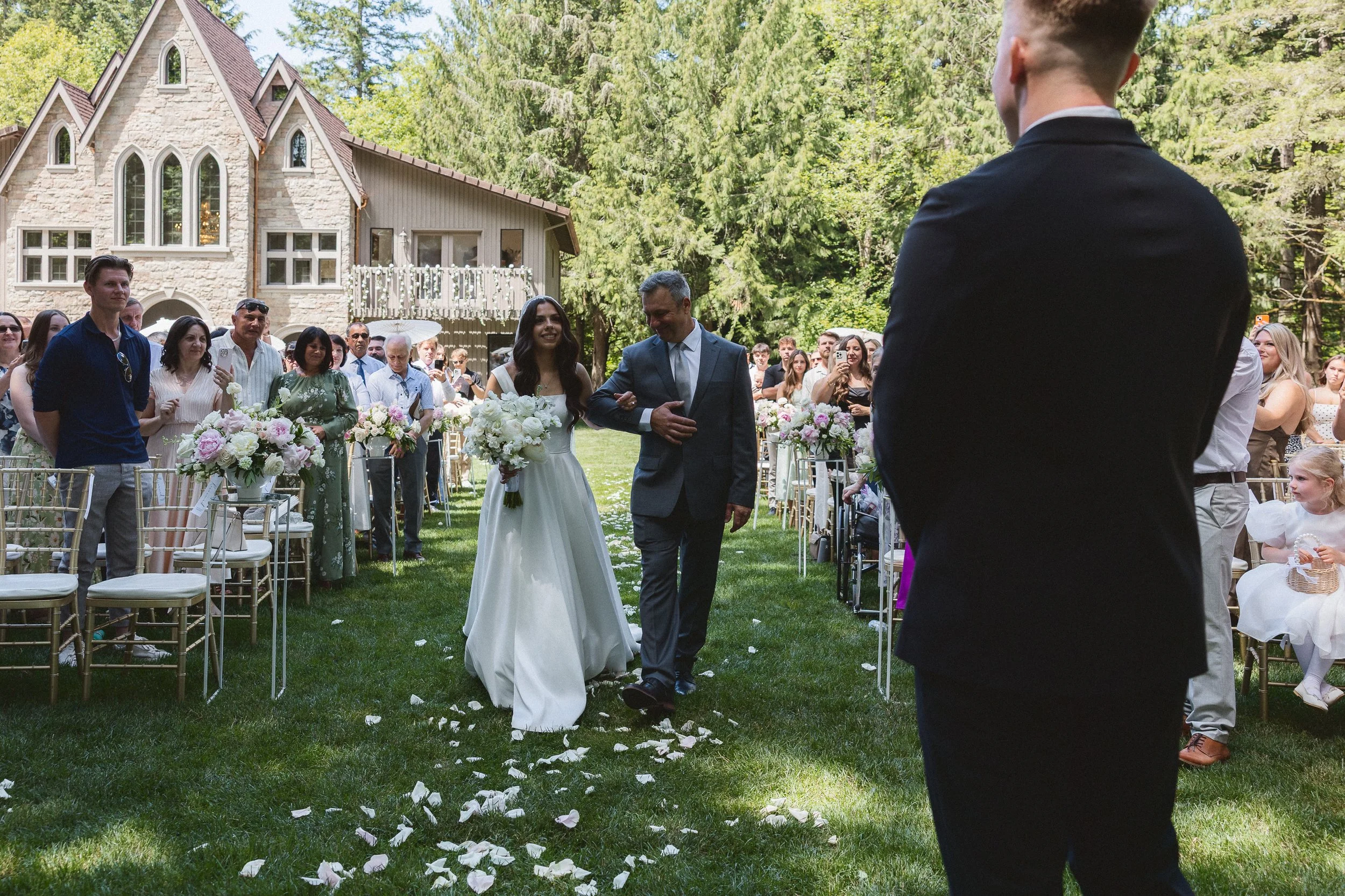 Bride walking down the aisle with her father as guests look on during the outdoor ceremony.