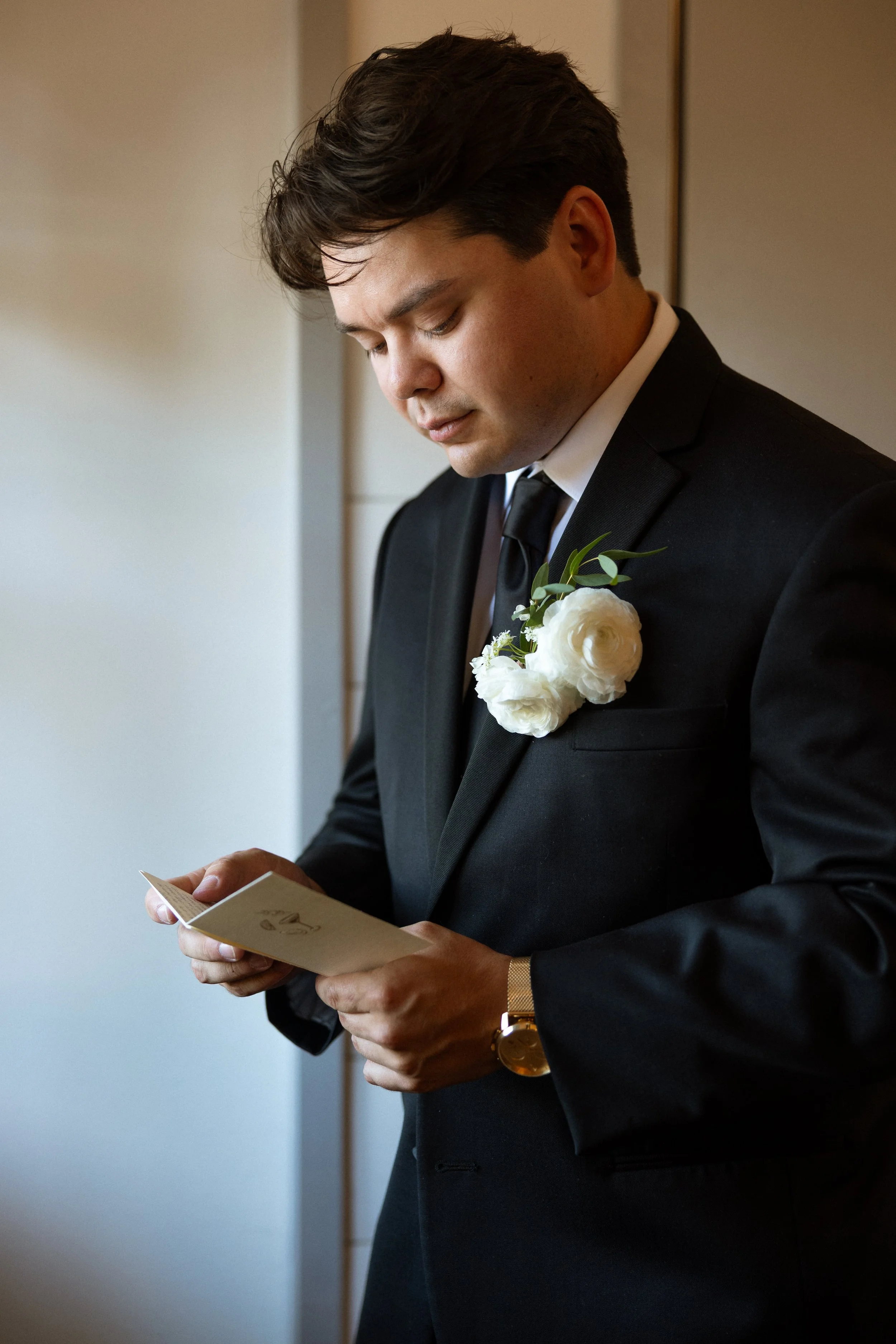 Groom reads a handwritten card by the window before the ceremony