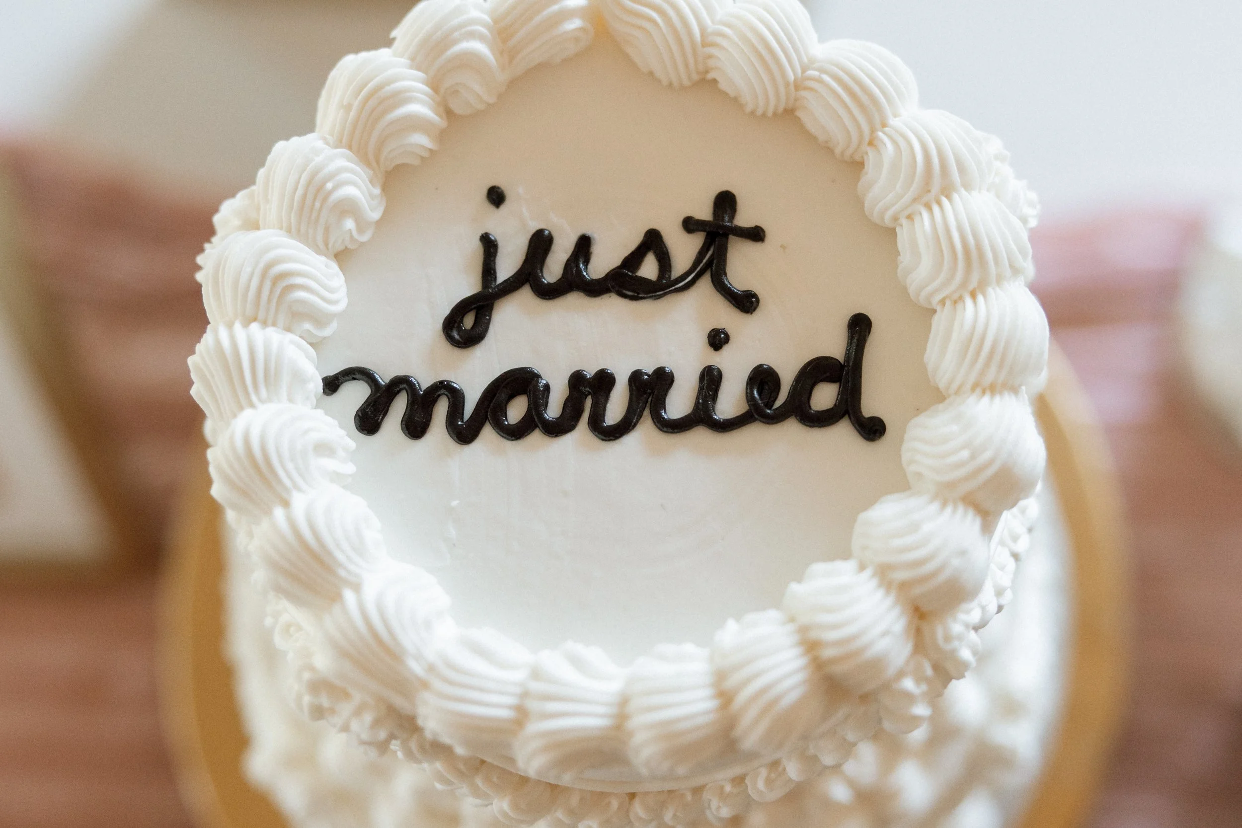White buttercream wedding cake lettered "just married" in dark script