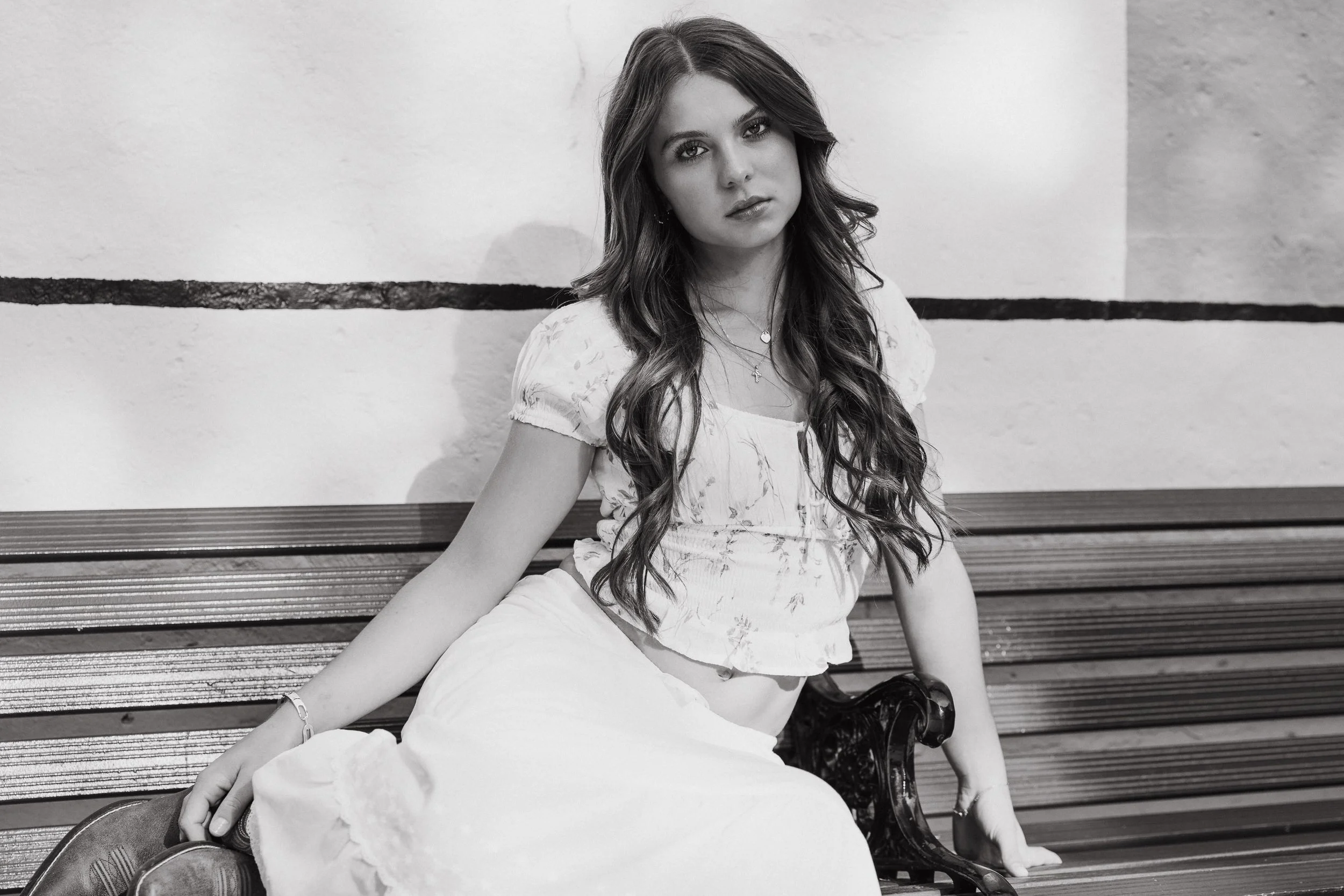 A black and white senior portrait of a young woman sitting on a bench at the historic San Juan Capistrano Train Station.